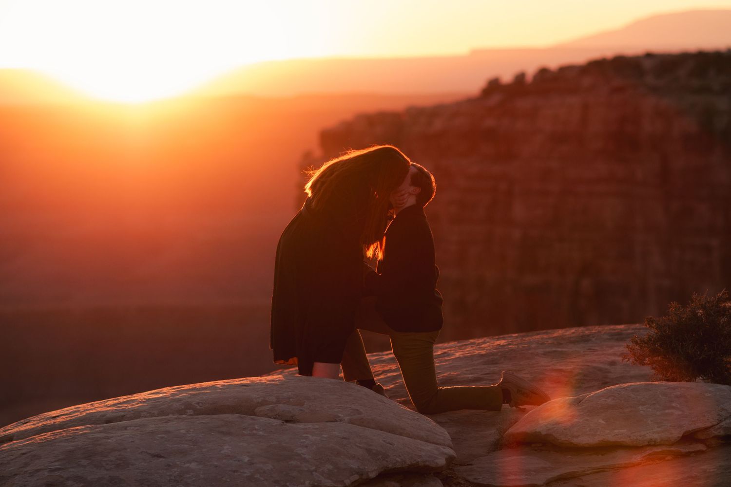 Dramatic silhouette of a couple during sunset on a mountain ledge.