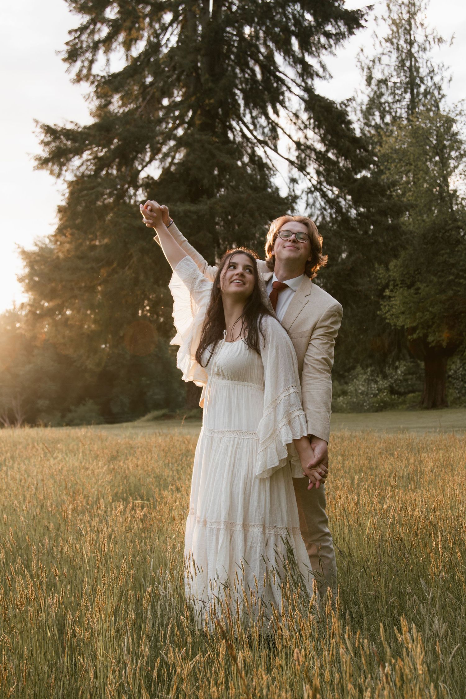 A joyful moment captured in a golden field during sunset with evergreens in the background.