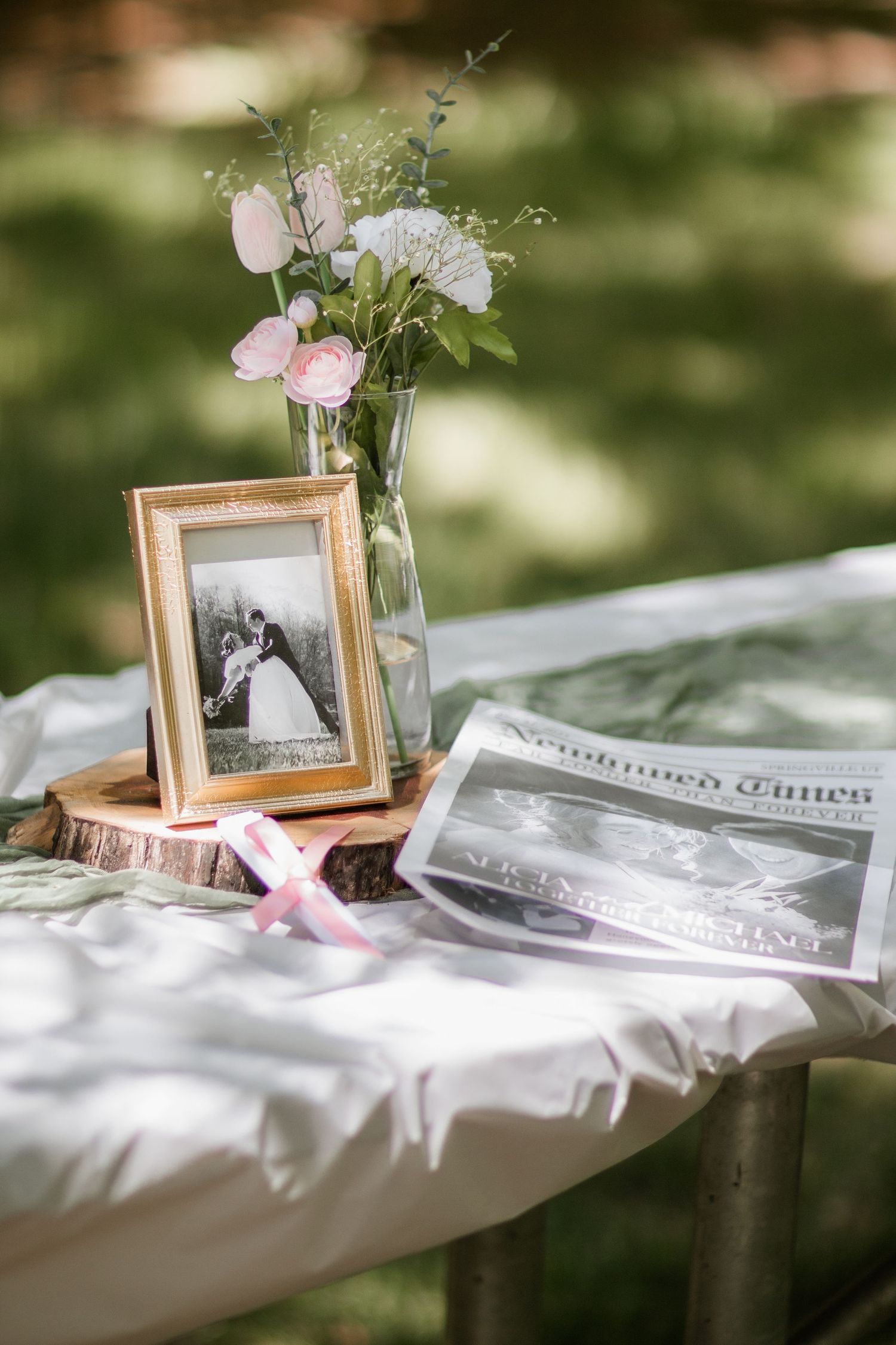 A vintage wedding photo in a wooden frame sits on a white tablecloth with delicate floral decorations.