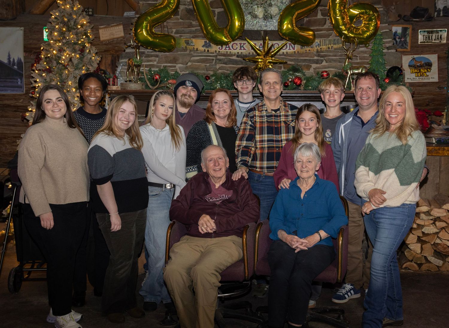 Large family portrait, multiple generations surrounding the eldest members sitting in front of a fireplace. Room looks warm and inviting.