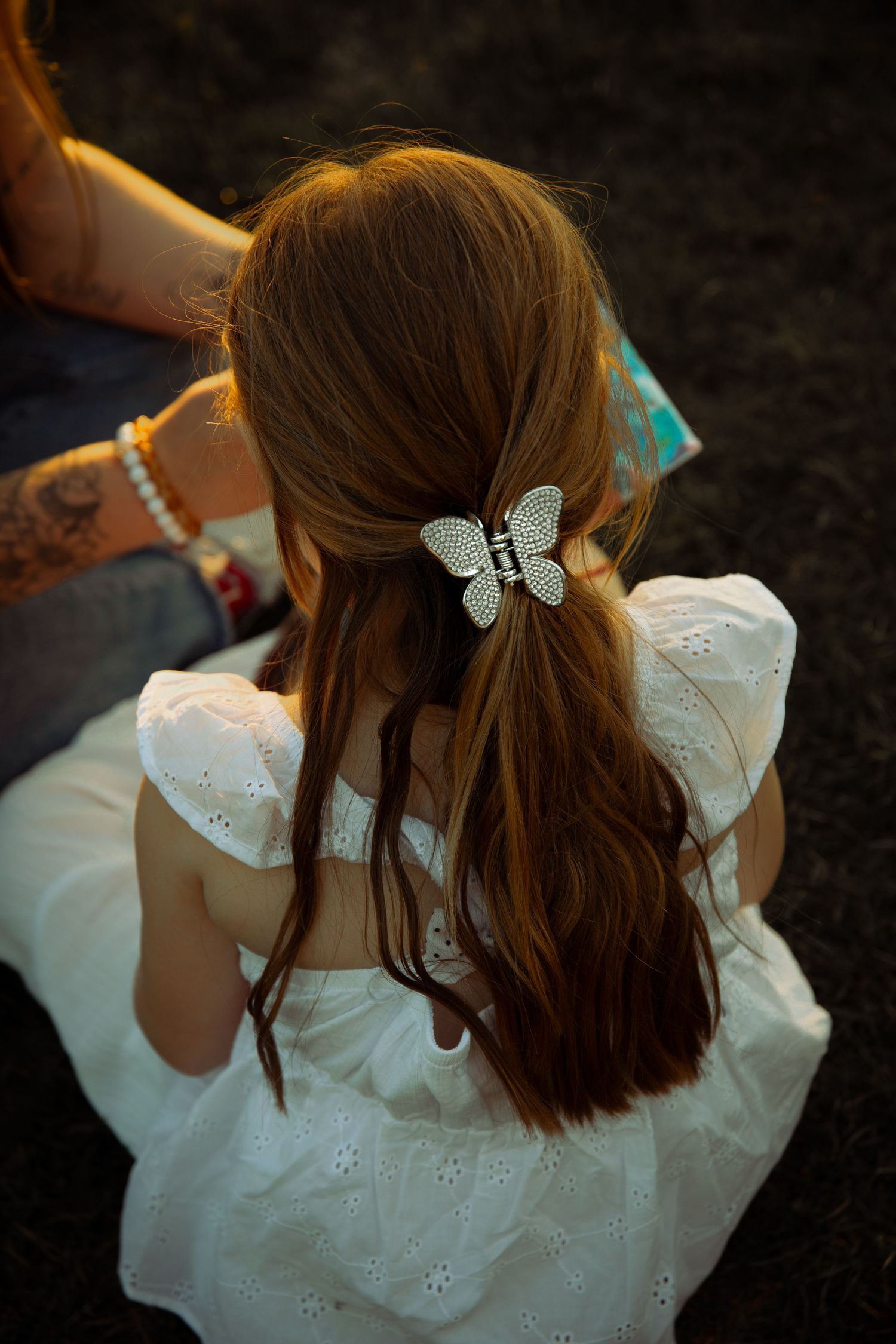 Portrait of child painting with mother at sunset in Missoula, Mt. Photo taken from back of head to showcase hairclip and curled hair.