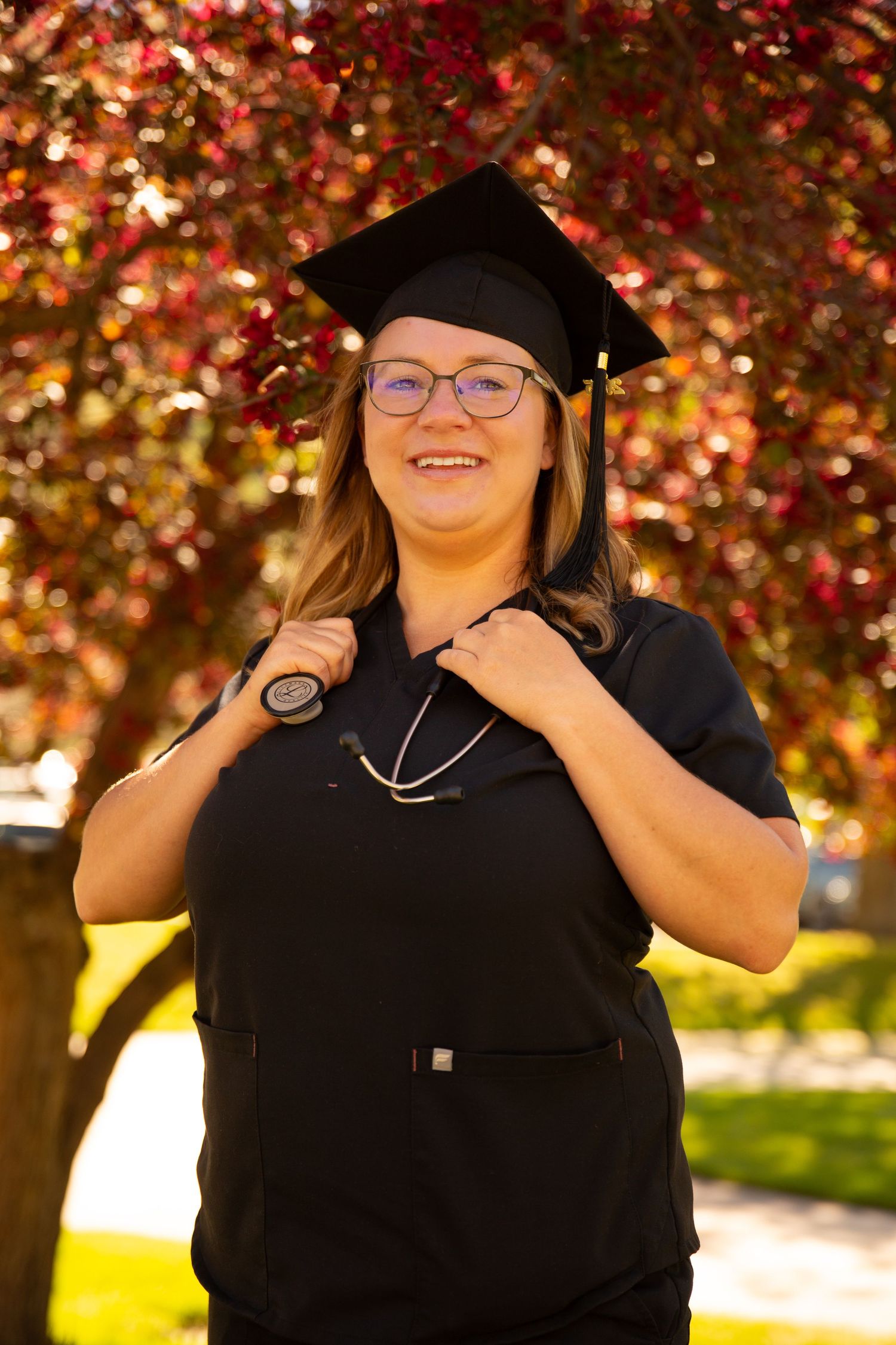 University of Montana nursing graduate holding stethoscope around neck. She is dressed in black scrubs, with a blooming tree in the back.