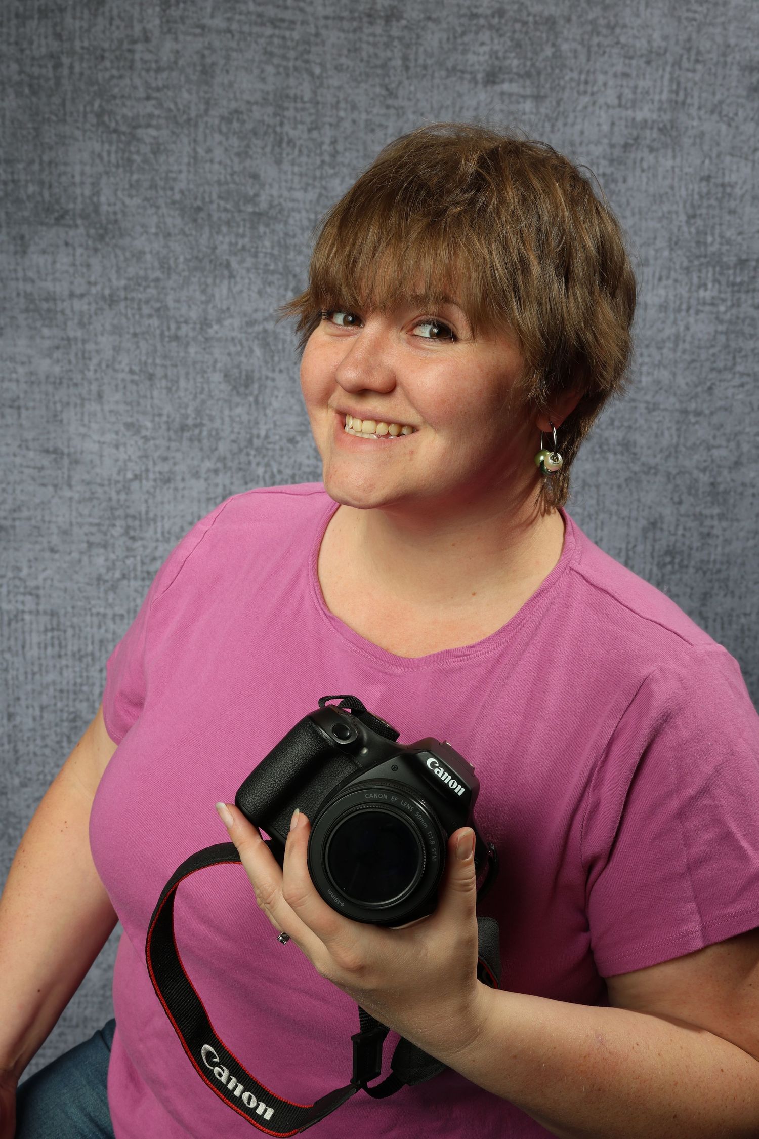 Image of Kayla from Kayla Sproles Photography LLC holding a canon dslr camera. Grey mottled background professional business portrait.