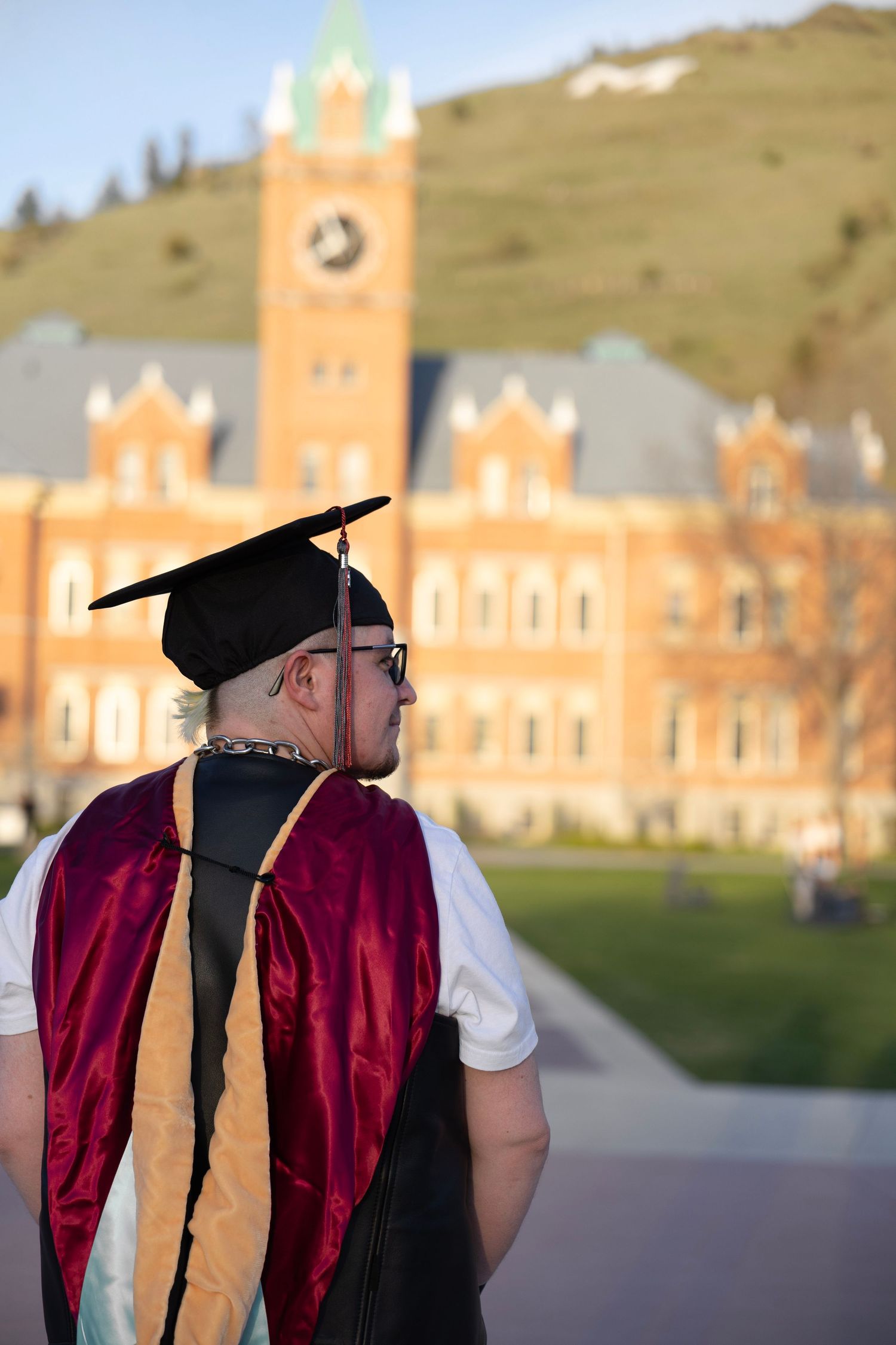 Graduate on the campus of the University of Montana, wearing black cap, maroon tassel, and master's hood for psychology.