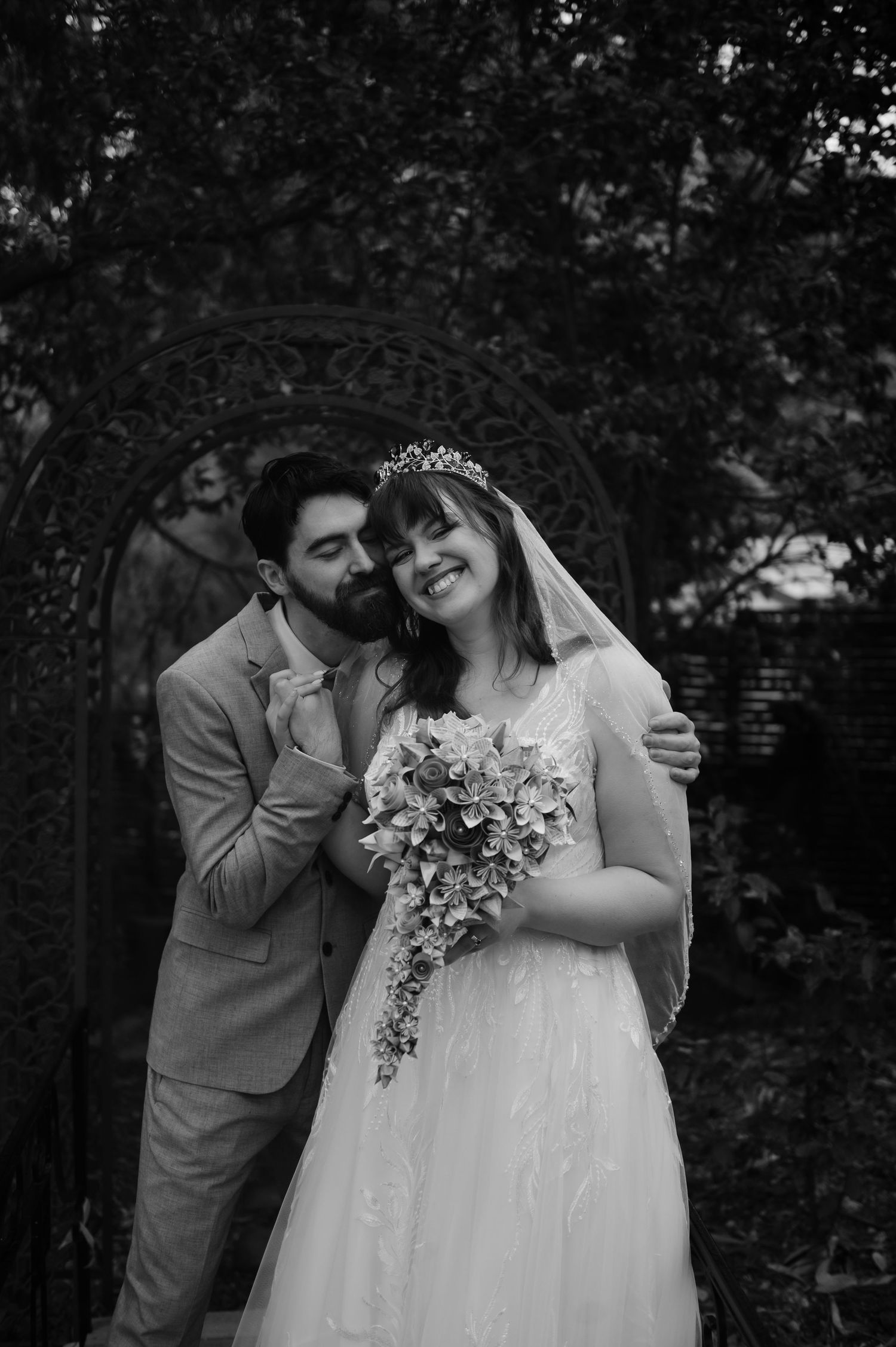 Black and white portrait of newlyweds sharing laughter with floral bouquet.