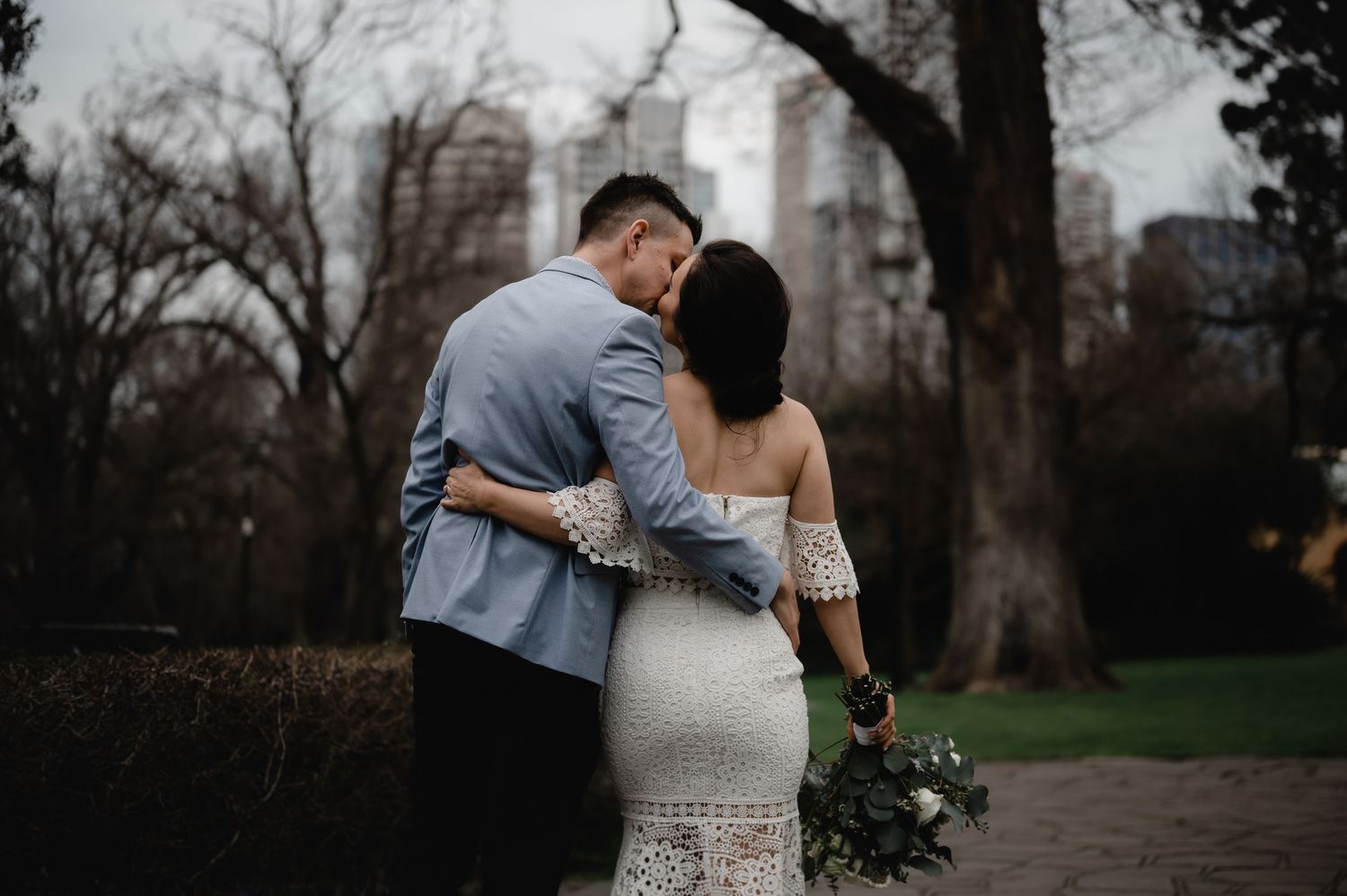 Intimate wedding portrait with city skyline visible through winter trees.