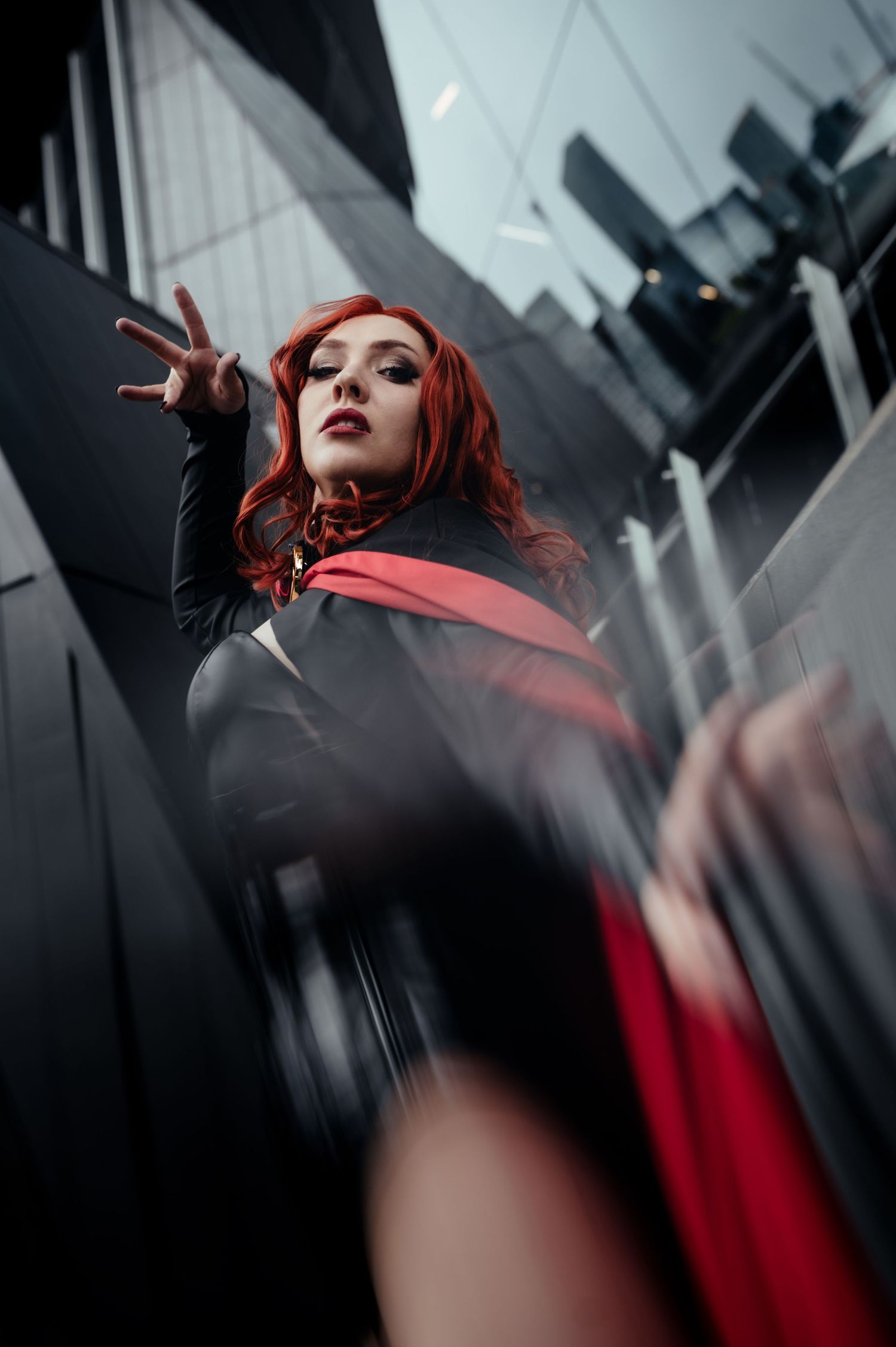 Dramatic low-angle shot of a cosplayer in red and black against modern architecture.