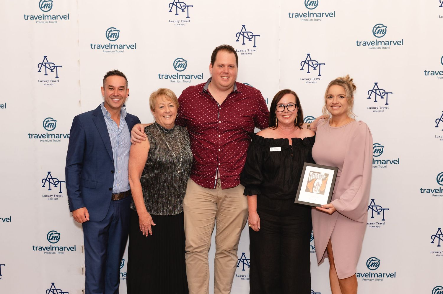 Group of five professionals posing together at a Travelmarvel awards event, one holding a framed certificate.