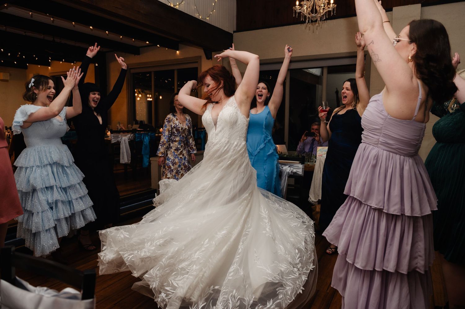 Wedding guests dancing in colorful dresses during a lively reception celebration.