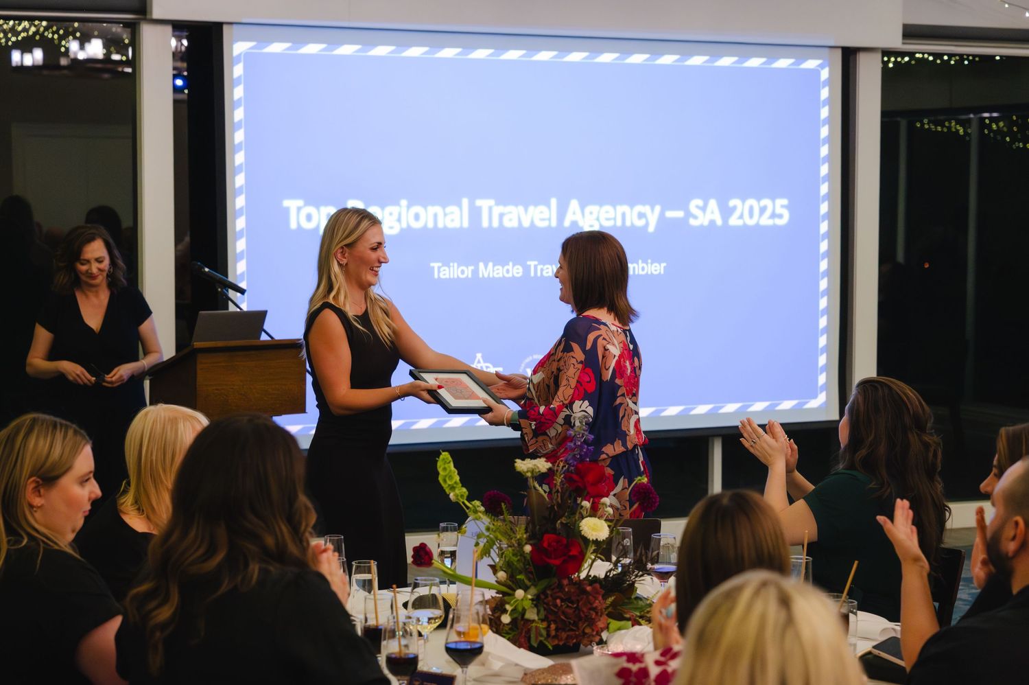 Two women exchange an award at the Top Regional Travel Agency SA 2025 ceremony during a formal dinner event.