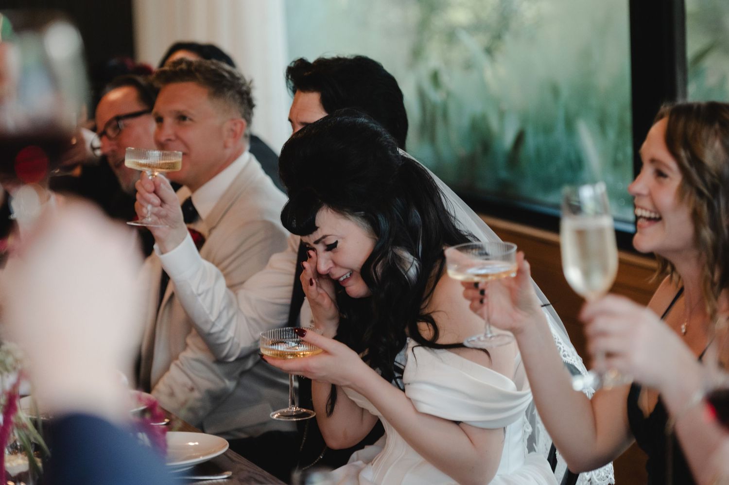 Wedding guests seated at tables enjoying a reception meal and conversation in a bright venue.