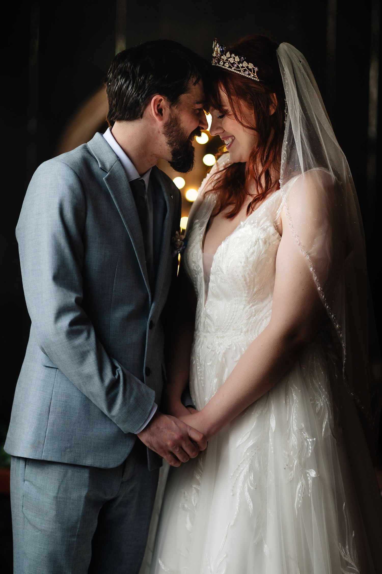 Intimate indoor portrait of couple in grey suit and white lace gown with dramatic lighting.