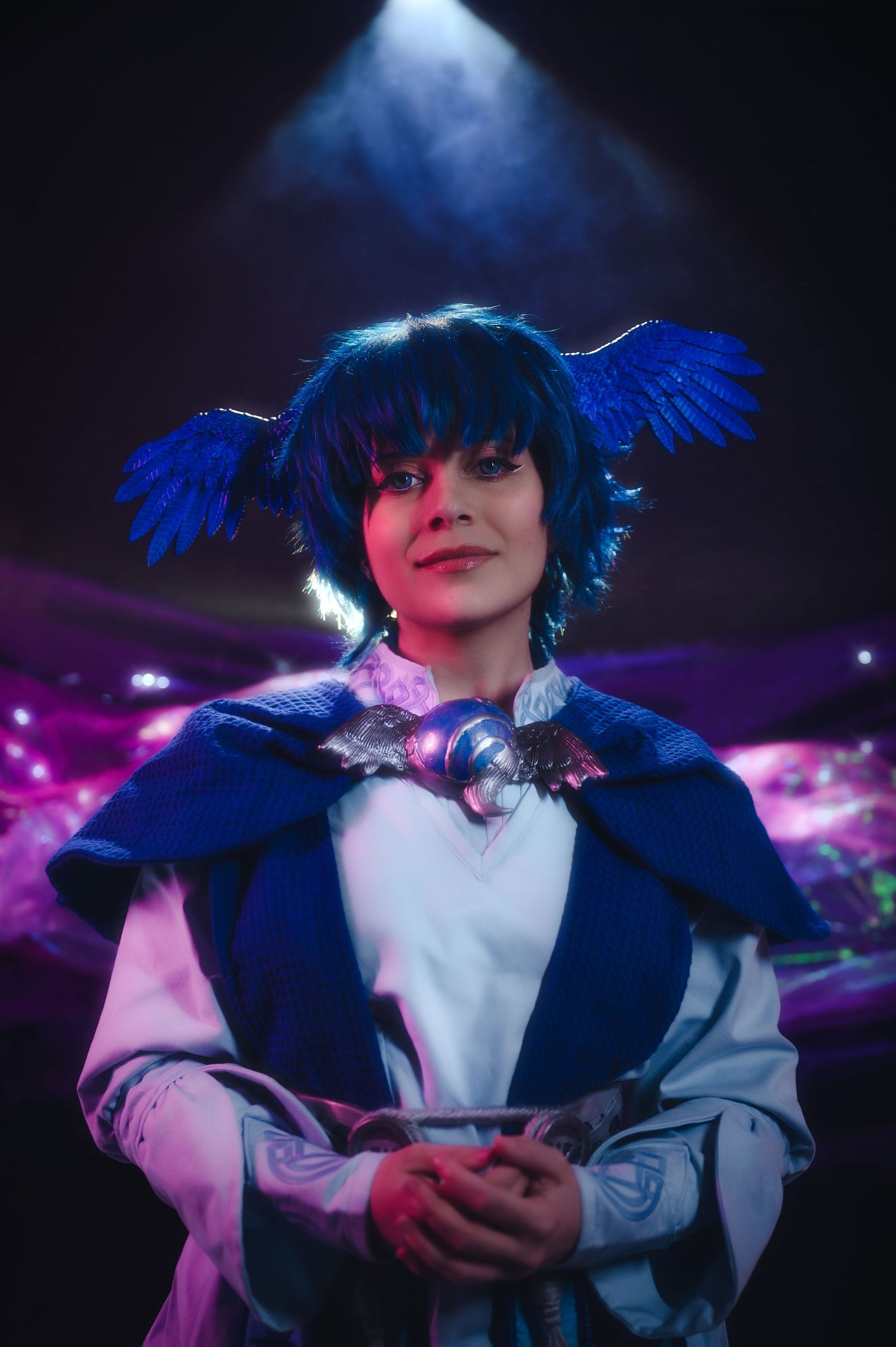 A cosplayer in a dark blue wig and white outfit poses dramatically against a moody purple-lit background.
