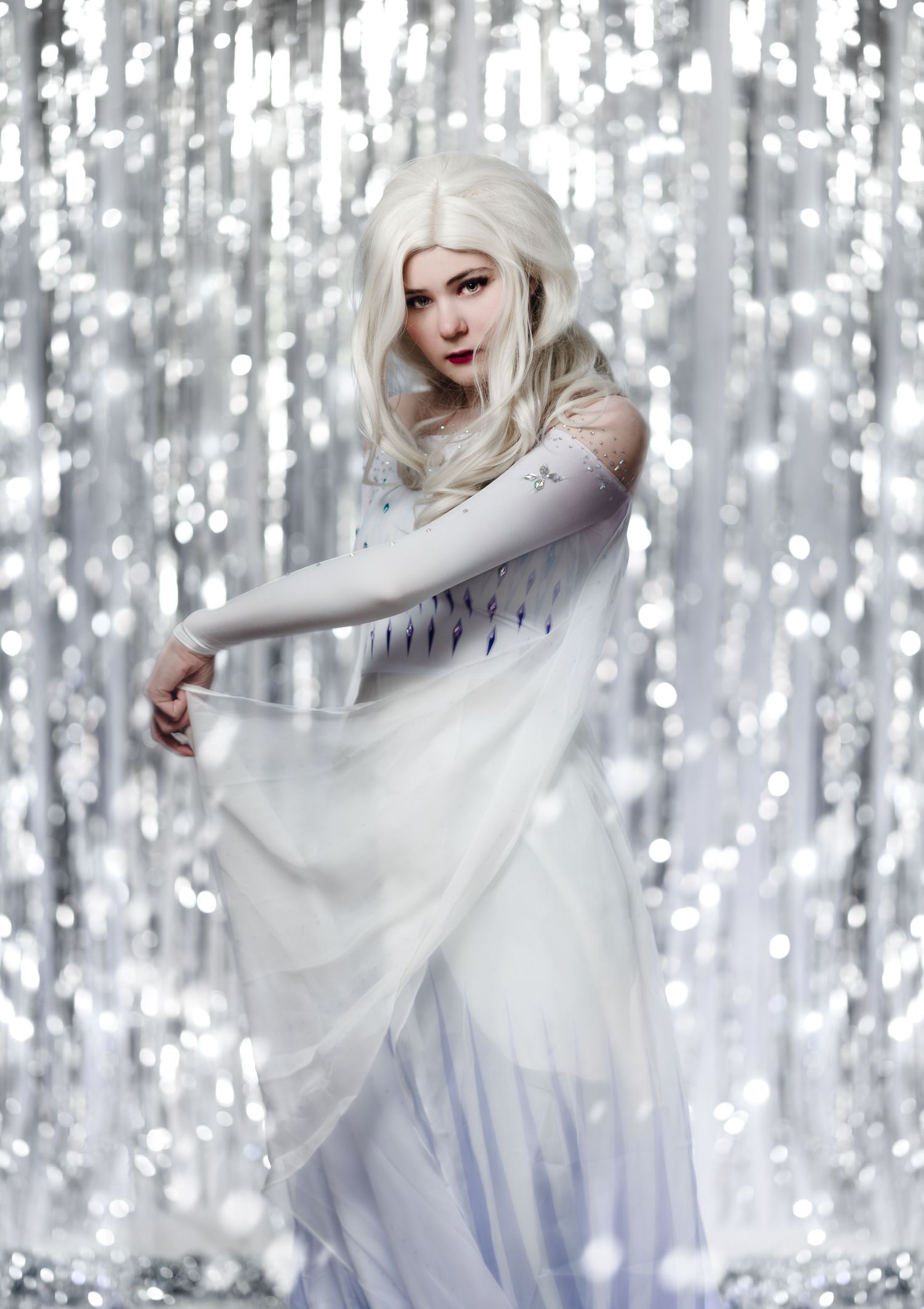 Ethereal figure in flowing white dress poses against a sparkling silver backdrop.
