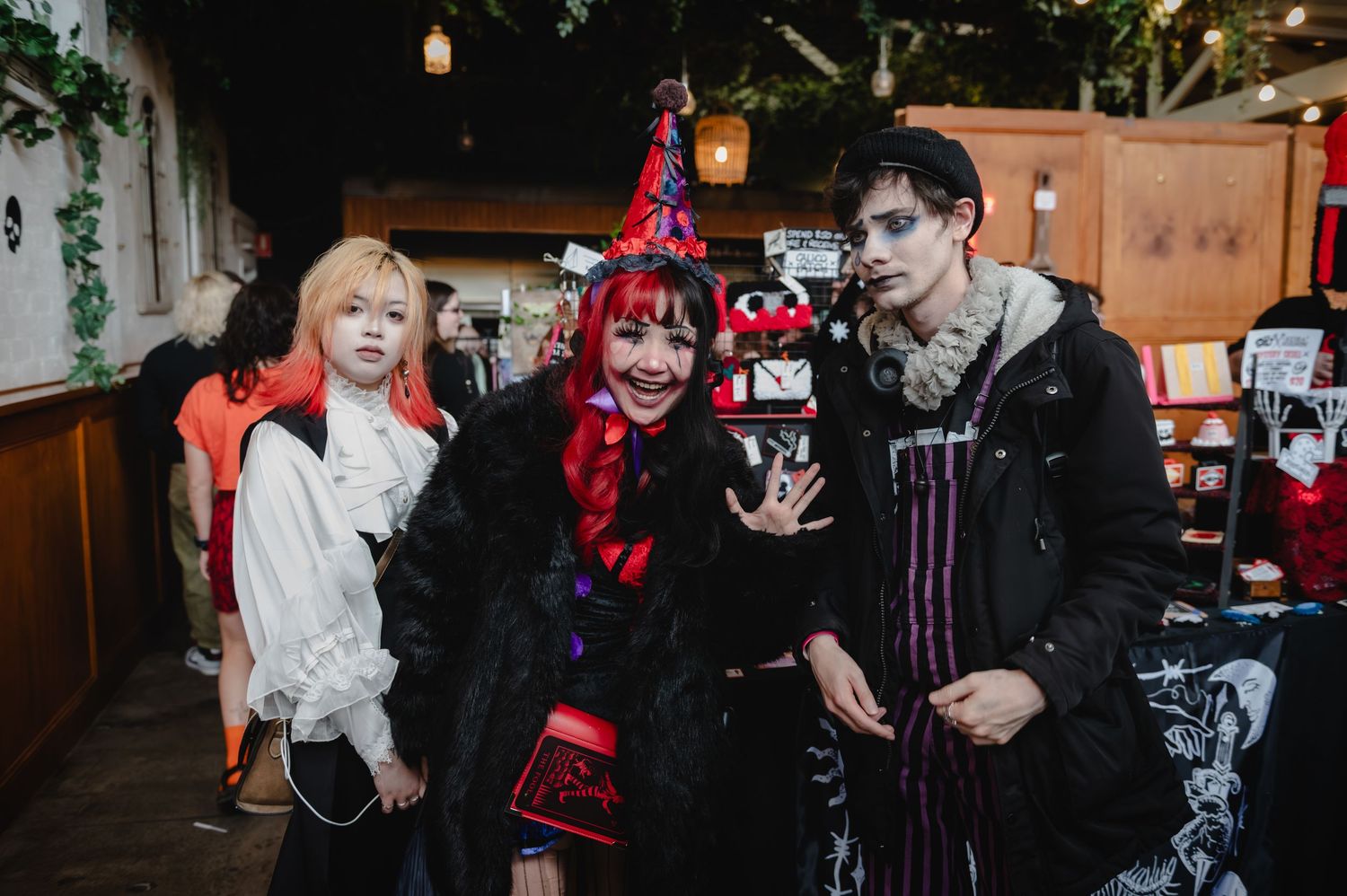 Three people in elaborate Halloween costumes pose together at a festive indoor event, wearing gothic and witch-themed outfits.