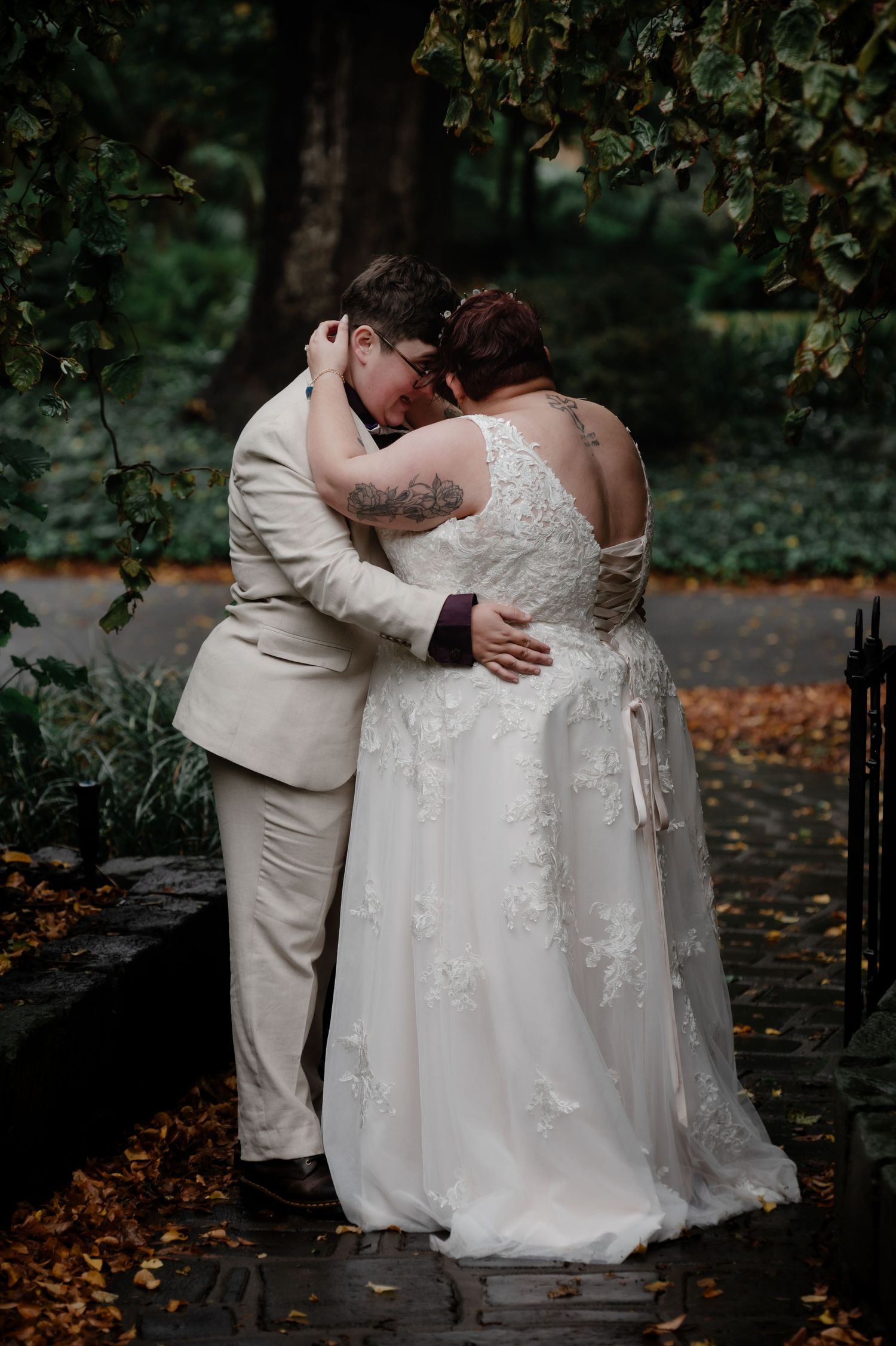 An intimate wedding portrait showing a couple in white and cream embracing on an autumn path.