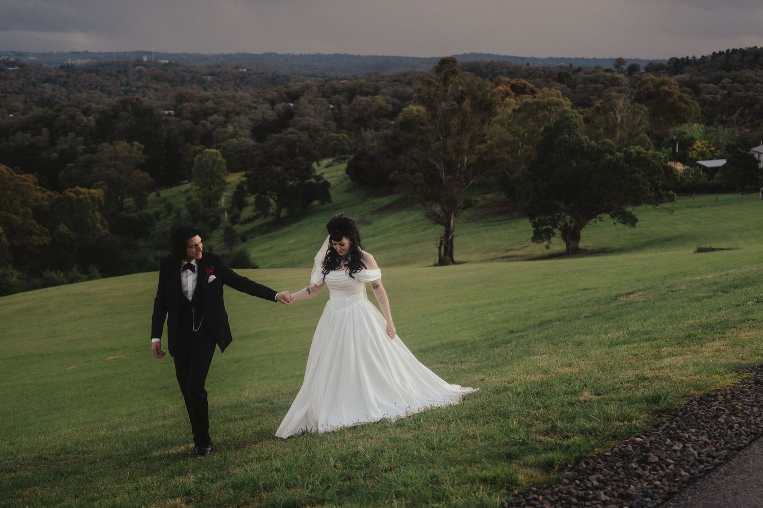 Bride and groom walk together across rolling green hills at sunset during an outdoor wedding photoshoot.