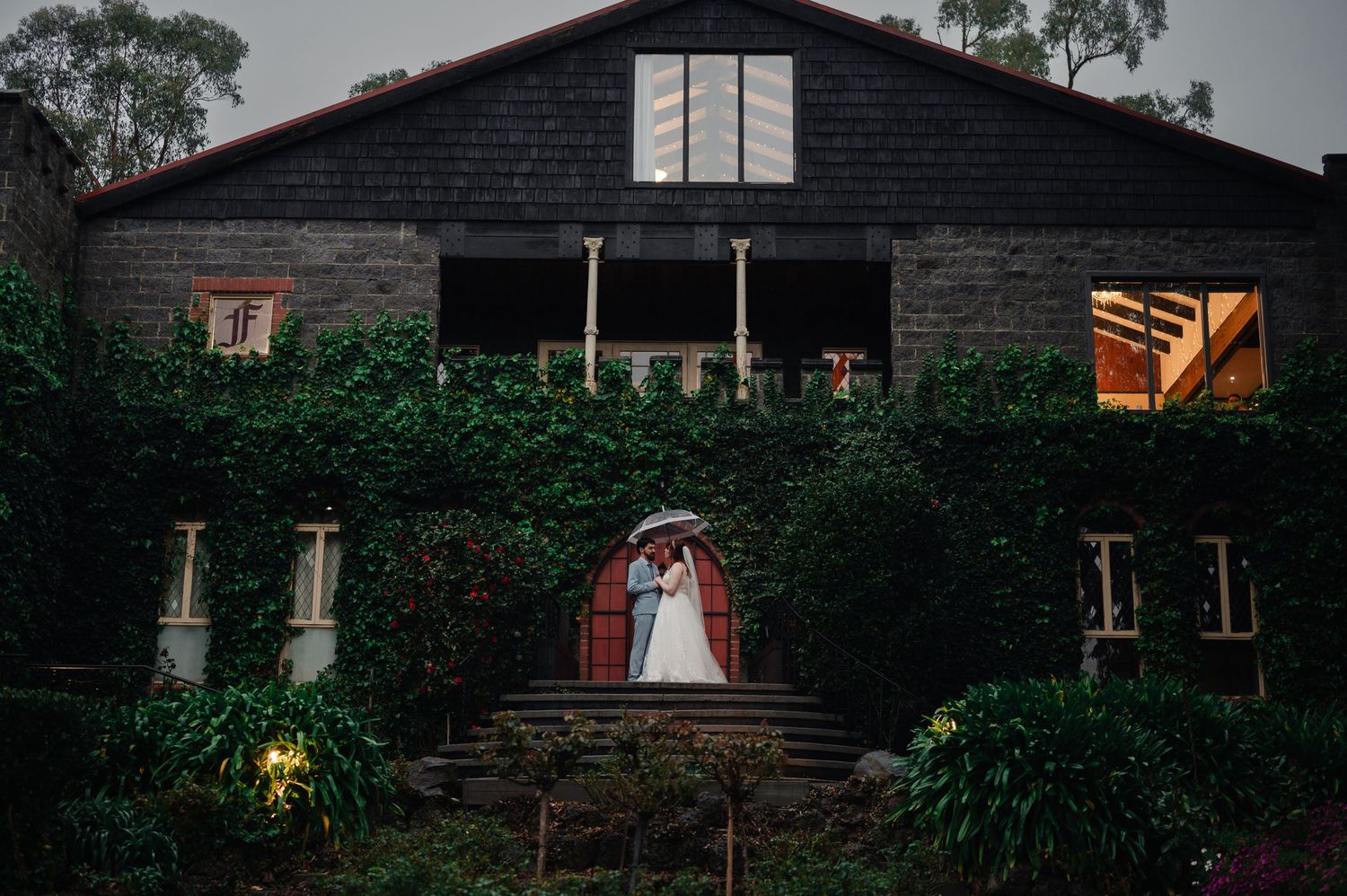 Dark wooden barn-style building exterior with windows and landscaping at dusk.