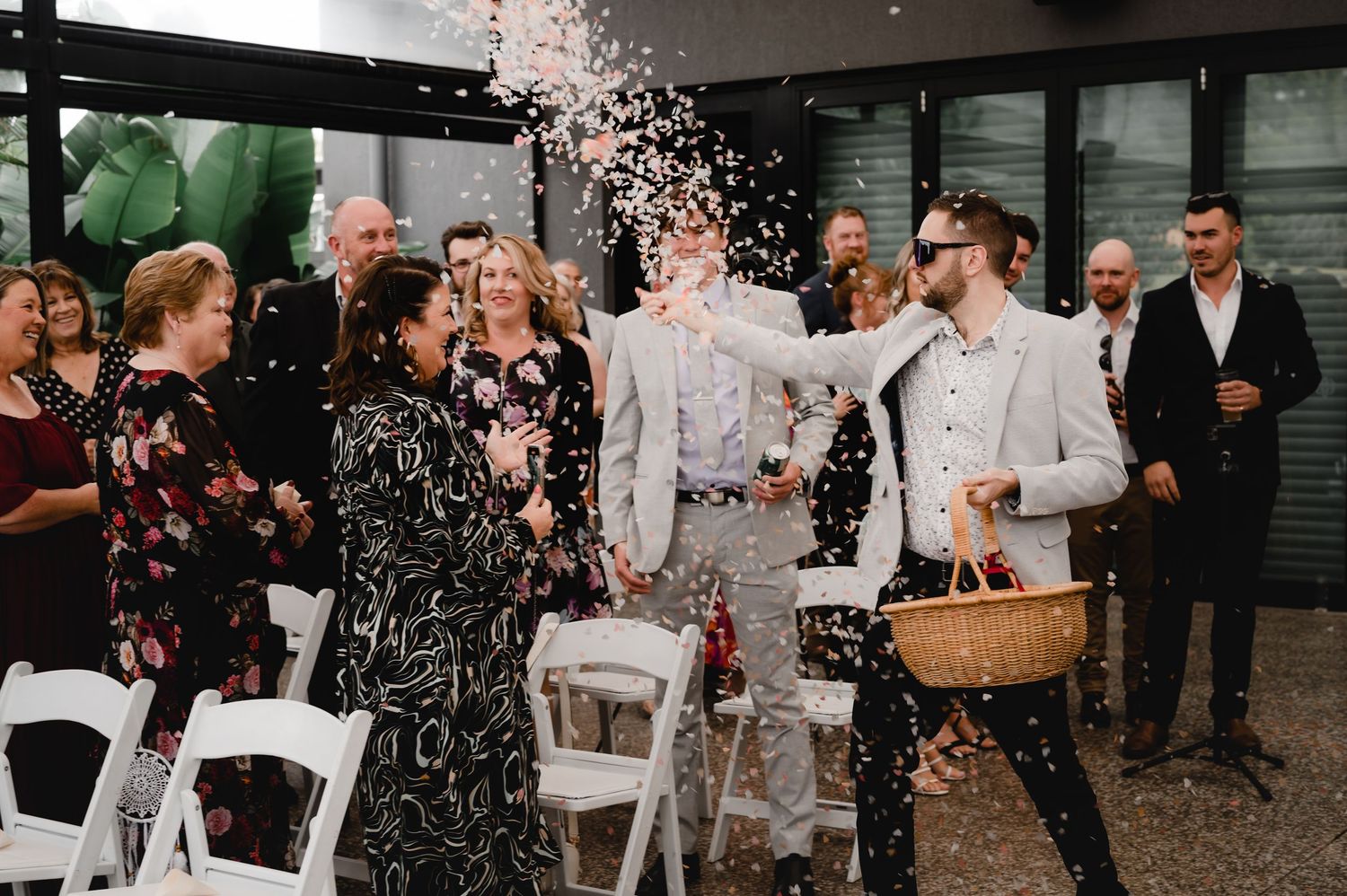 Wedding guests celebrate with confetti during an outdoor ceremony with white chairs.