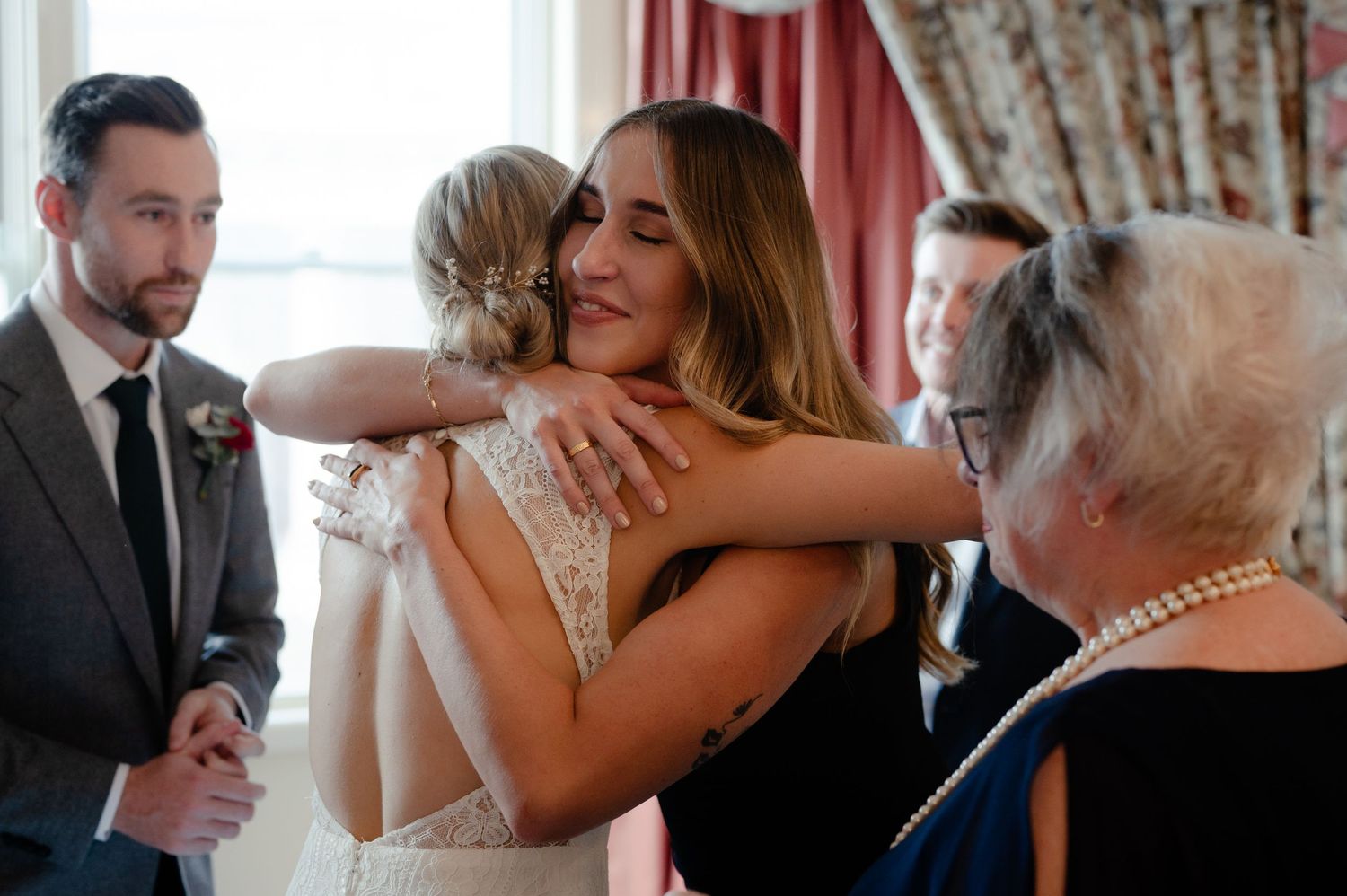 Wedding celebration with guests sharing emotional embraces in a sunlit room.