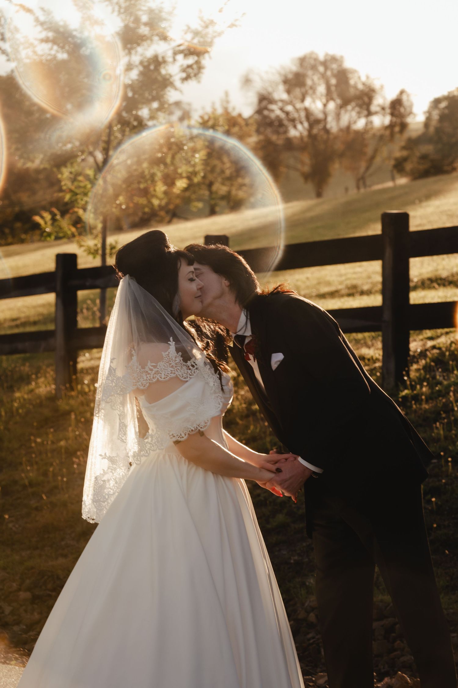 Sunset wedding portrait with golden light streaming through a rustic fence.