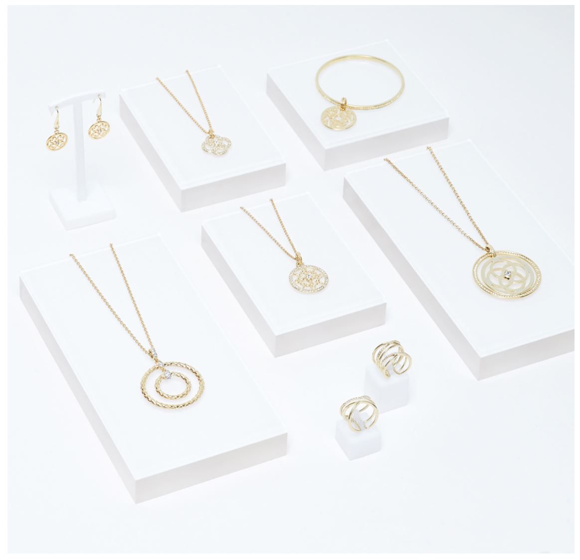 Gold-tone jewelry set featuring circle pendant necklaces, hoop earrings, bangle bracelet, and rings displayed on white risers.
