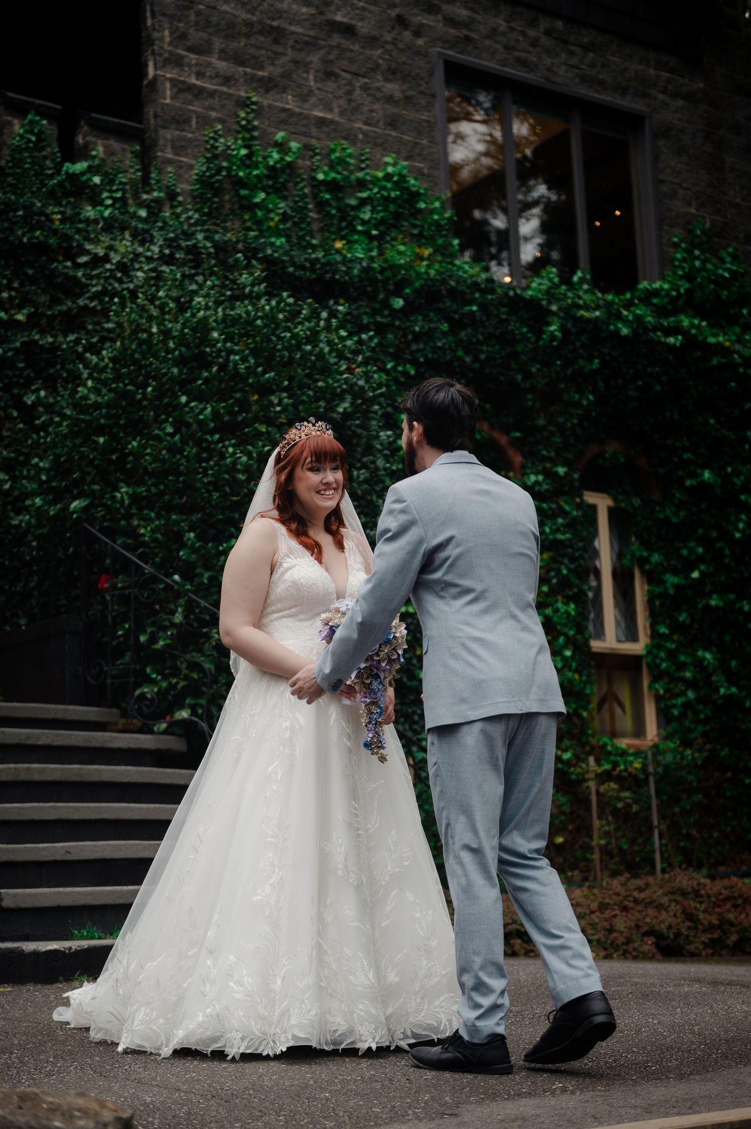 Wedding couple shares a tender moment on stone steps surrounded by ivy-covered walls.
