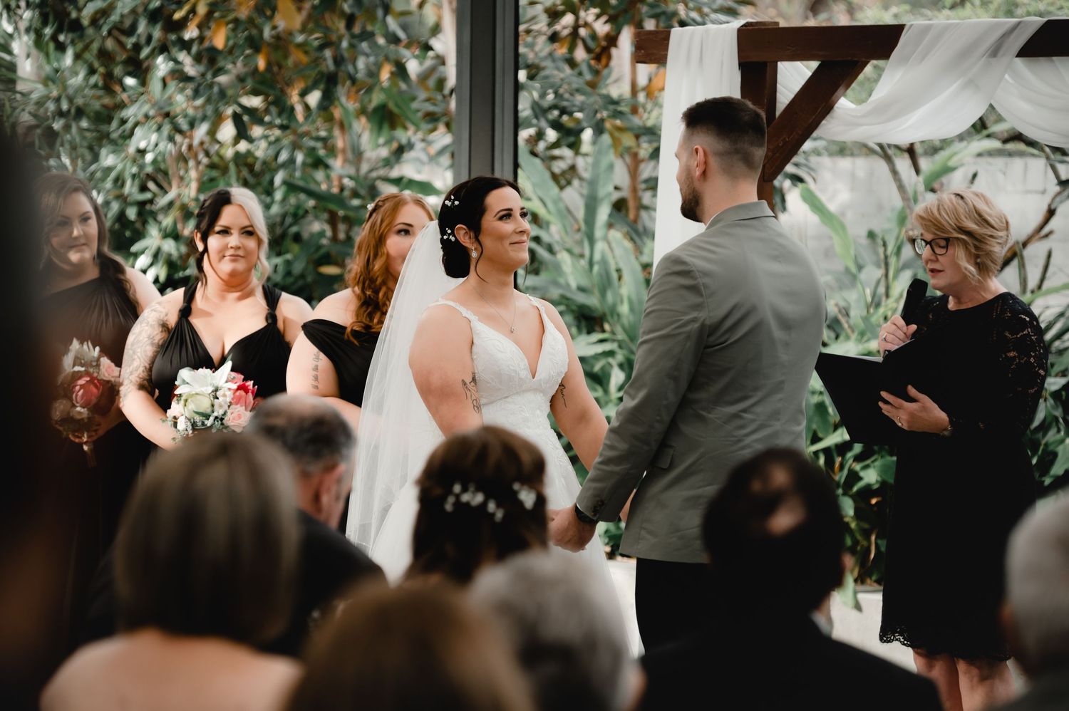 Wedding ceremony taking place in an elegant indoor venue with greenery and natural light.