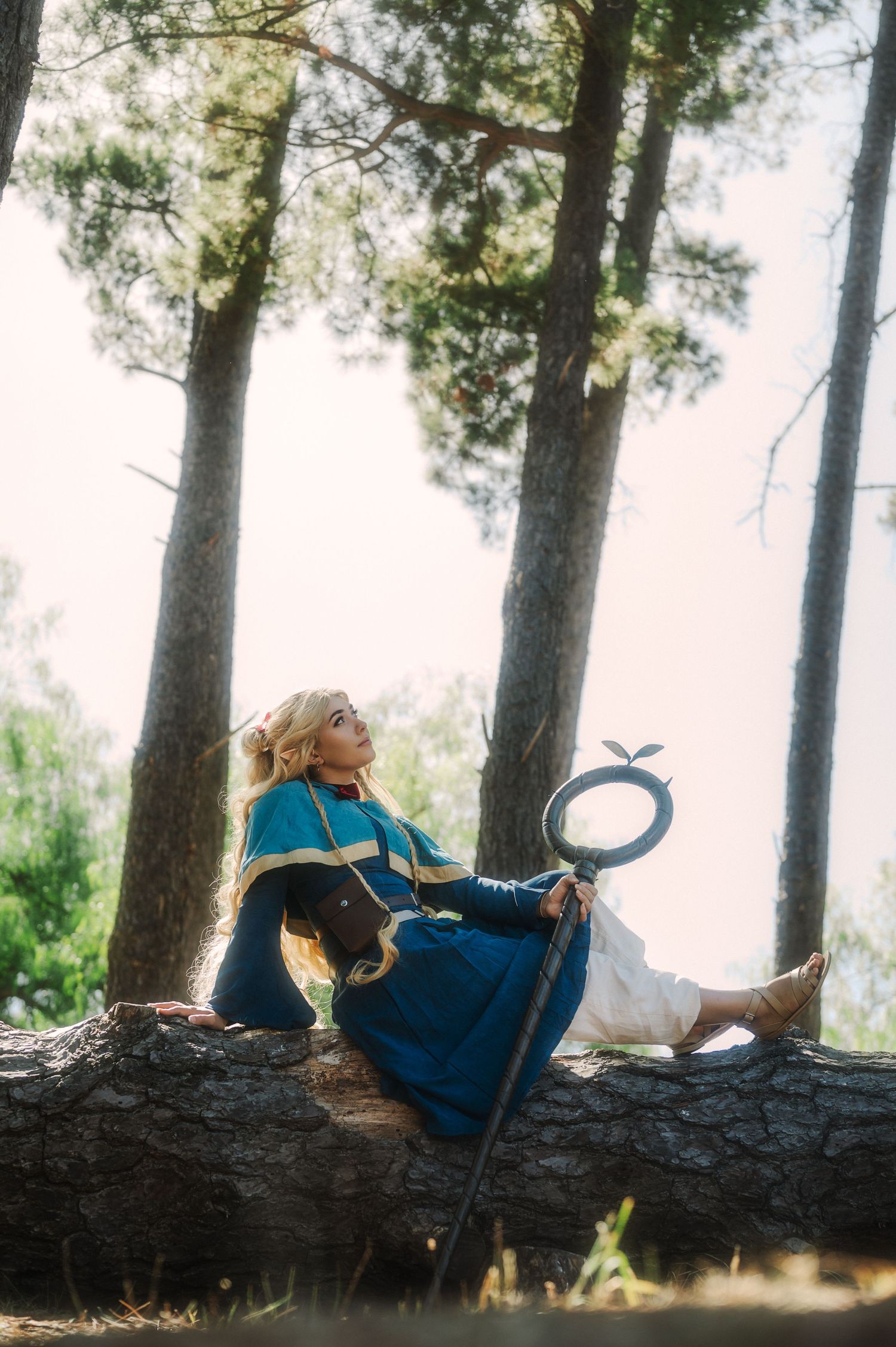 Whimsical forest cosplay scene with someone resting on a fallen tree trunk holding a mirror.