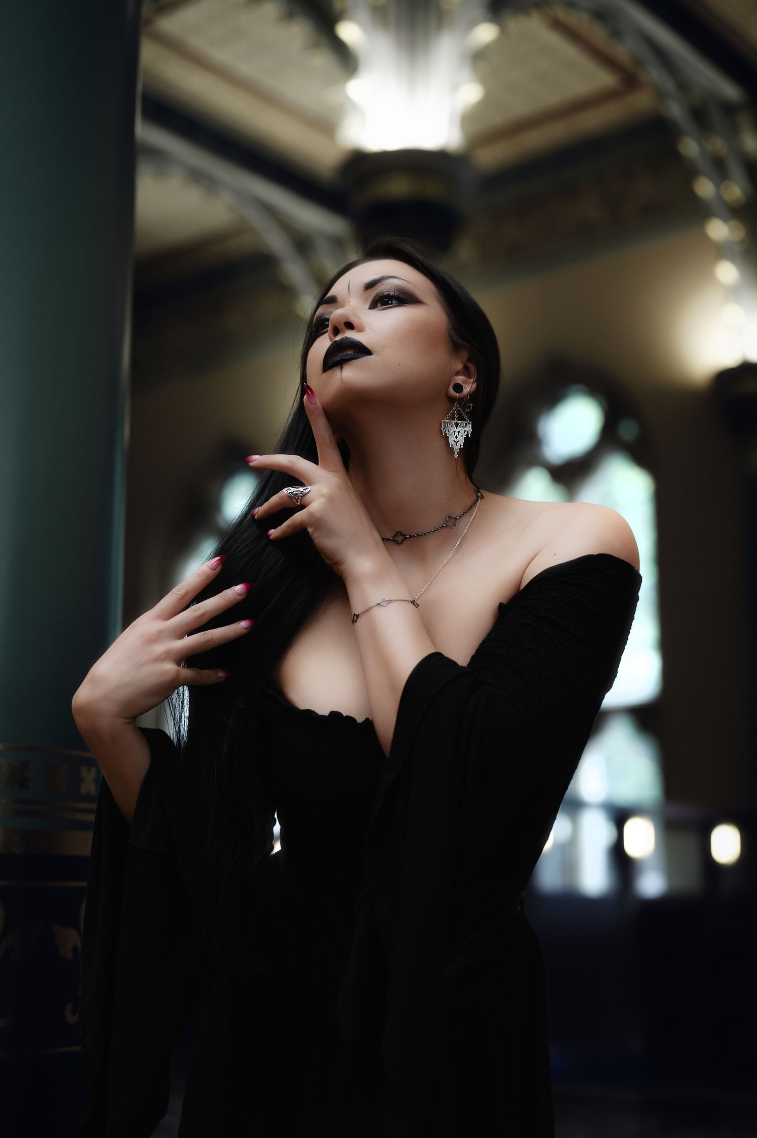 Dramatic portrait in black off-shoulder dress with dark lipstick in ornate interior setting.