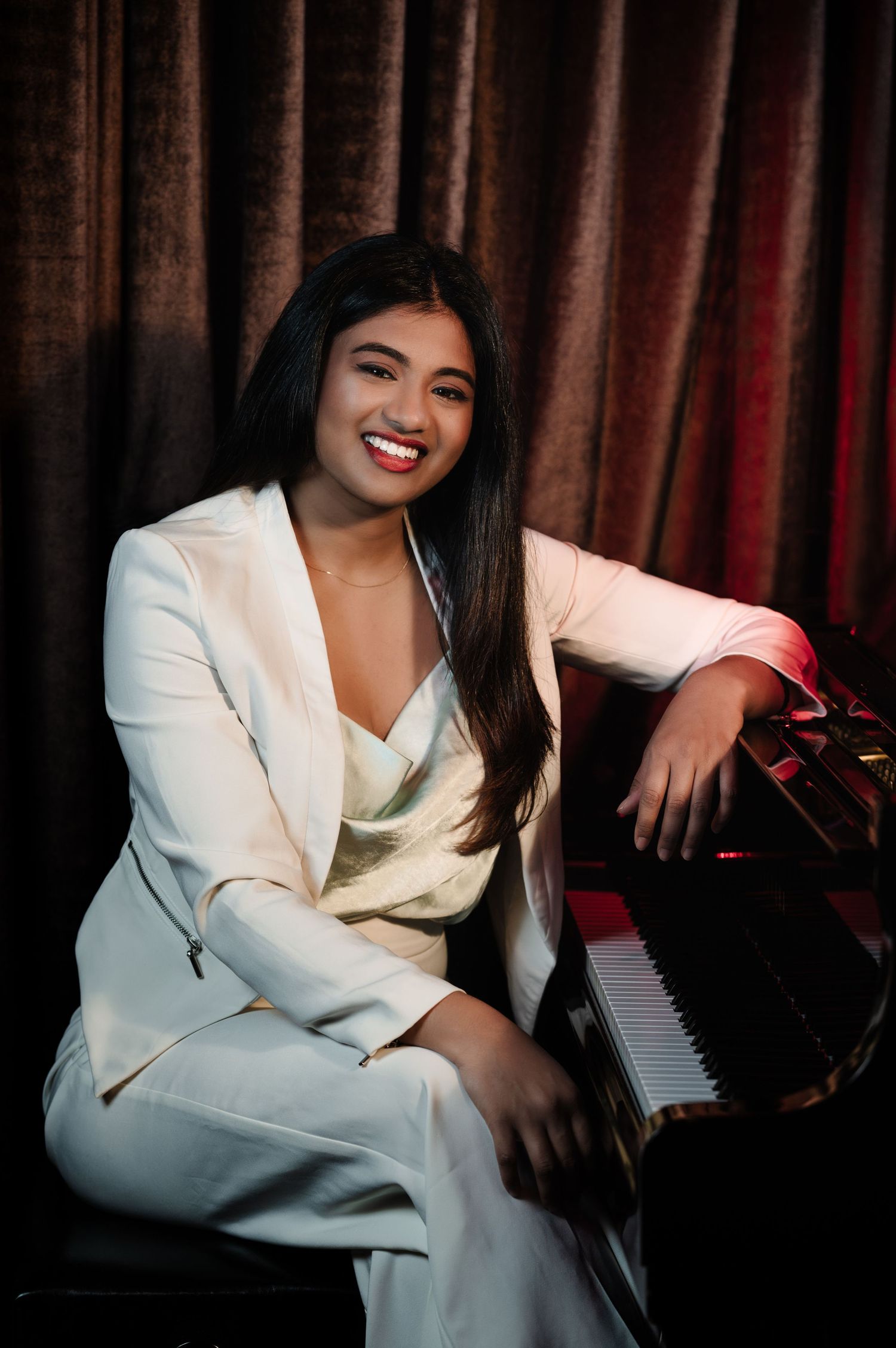 Glamour photoshoot of pianist in white suit sitting at piano with dramatic lighting.