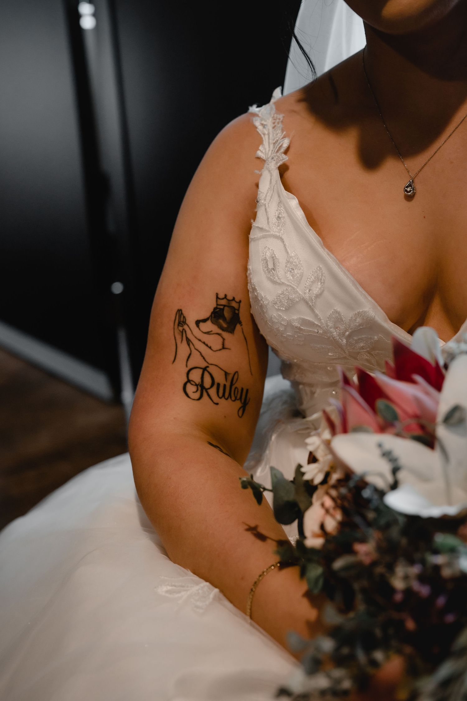 Close-up of a bride's arm showing delicate tattoo details against white wedding dress.