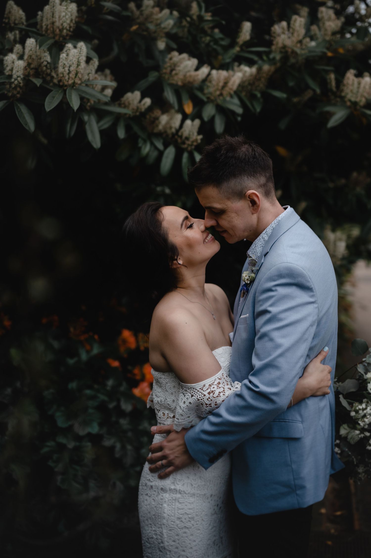 Intimate wedding moment captured under flowering trees in moody lighting.