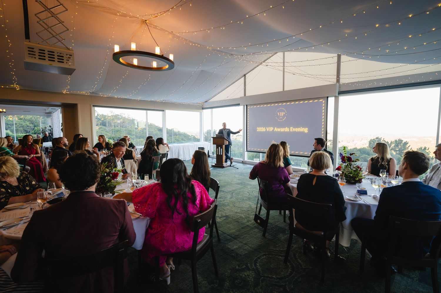 Guests seated at round tables during a formal awards evening in an elegant venue with panoramic views.