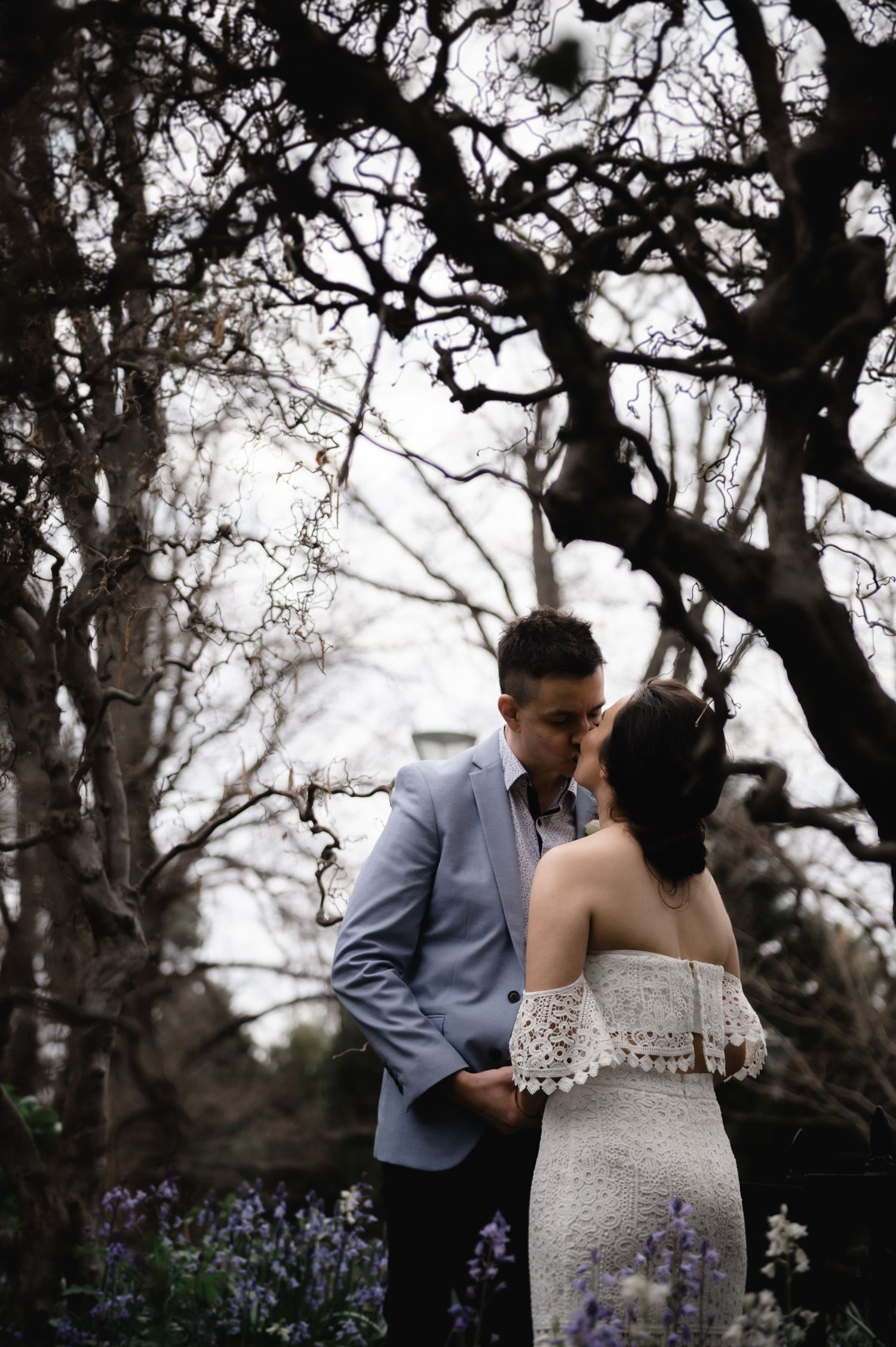 Romantic wedding portrait under dramatic tree branches with moody lighting.