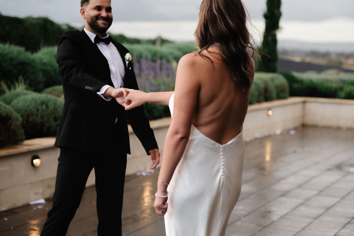 Wedding couple dances and laughs together on outdoor terrace with vineyard views.