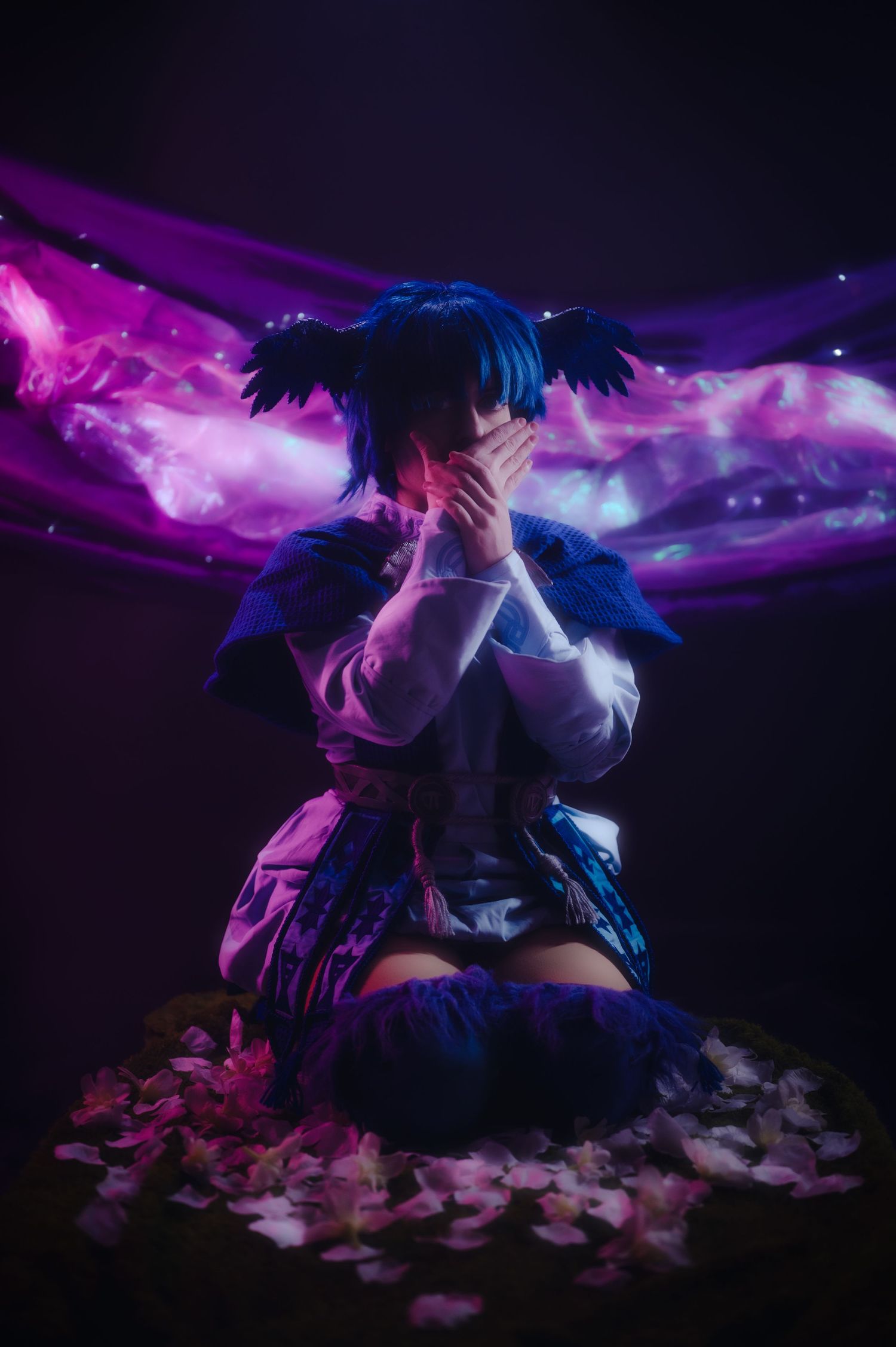 Artistic portrait with flowing fabrics in purple and blue lighting against a dark background.
