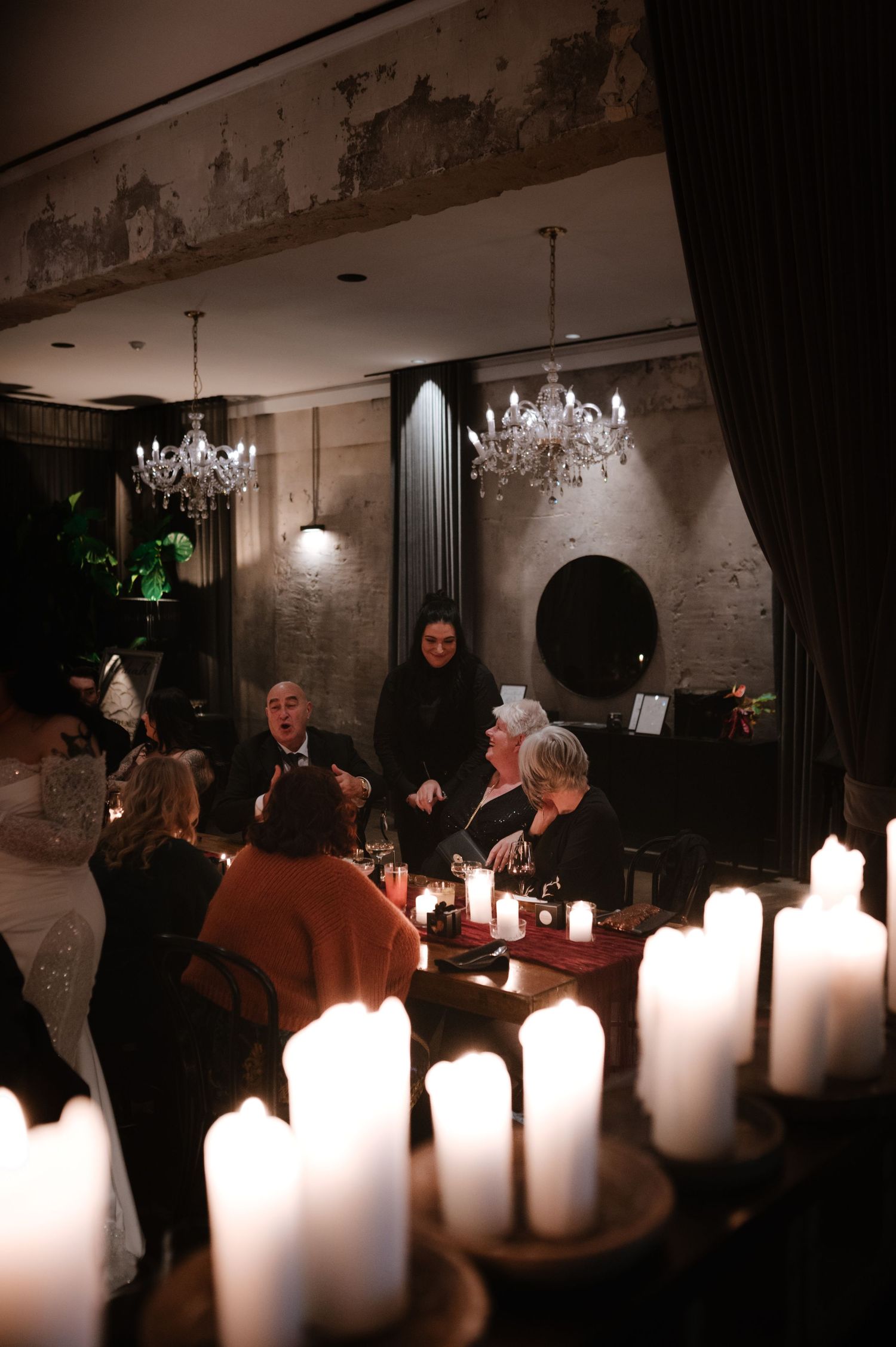 Dark reception venue illuminated by white pillar candles with crystal chandeliers overhead.