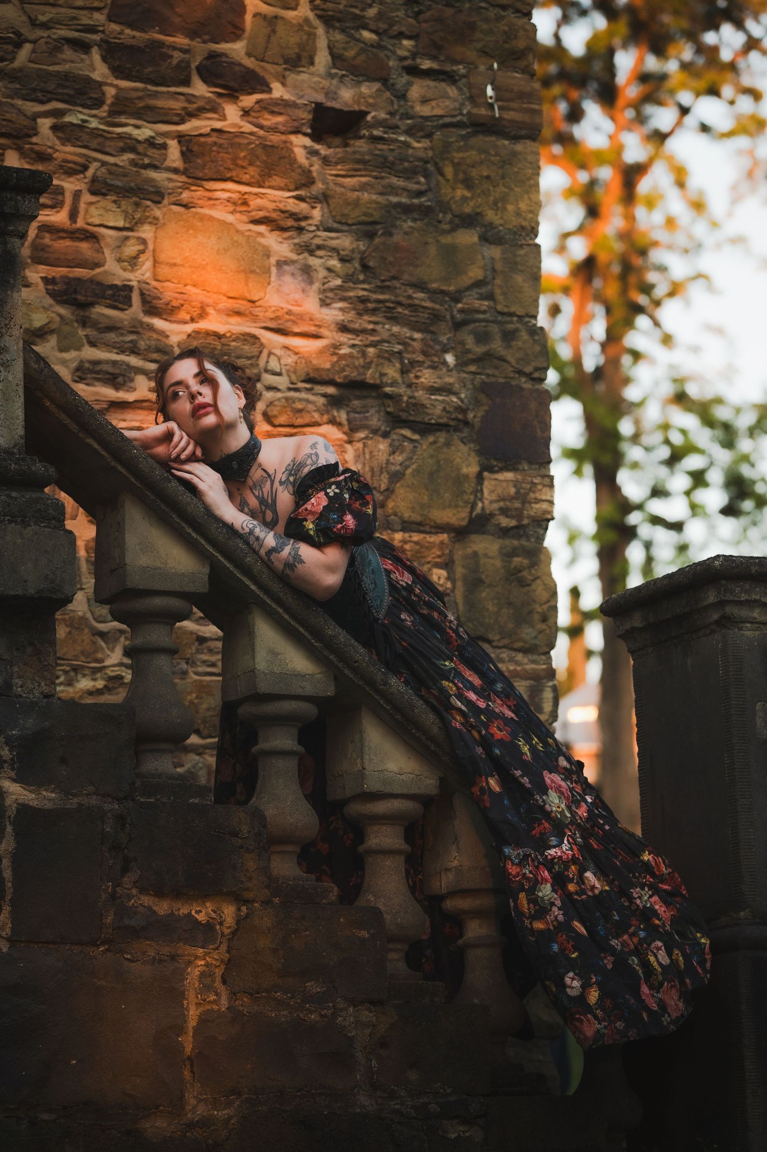 A figure in a floral dress reclines dramatically on stone steps at sunset.