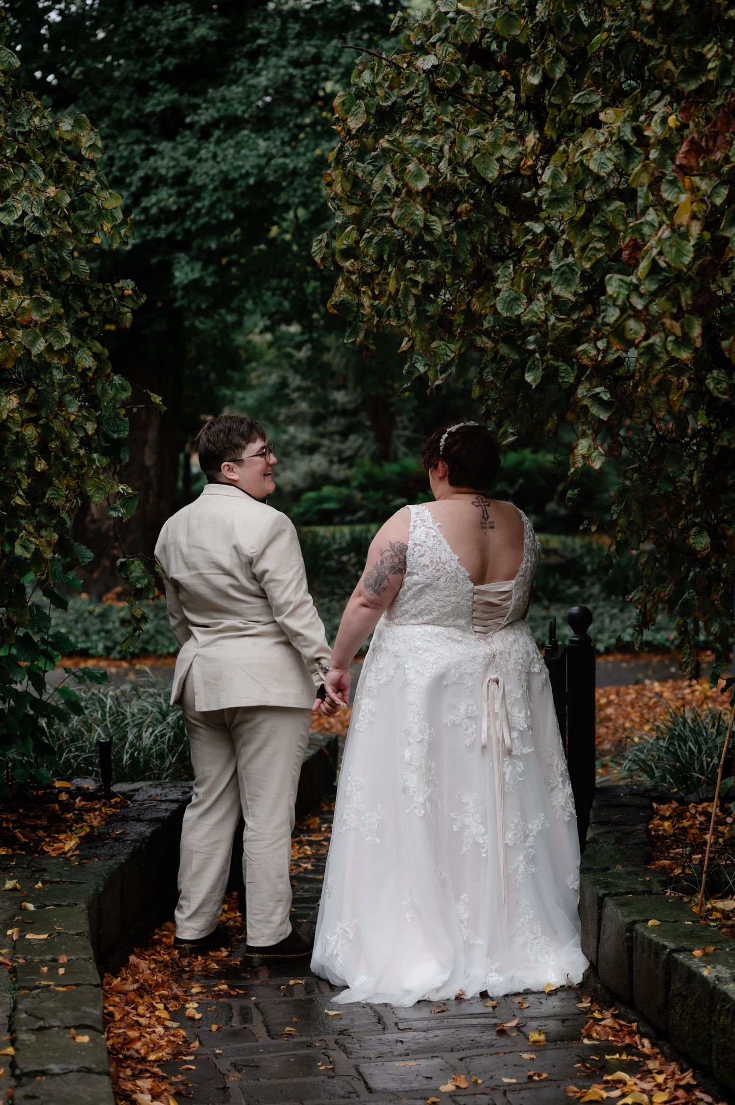 Newlyweds sitting on stone wall surrounded by autumn foliage in matching white and cream outfits.