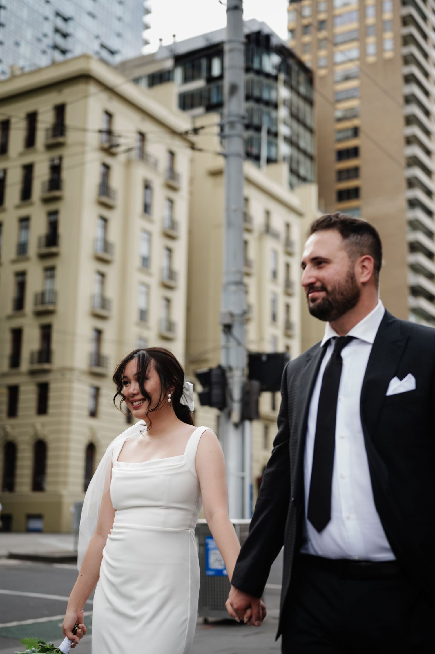 Urban wedding photos with couple walking along city street with tall buildings.