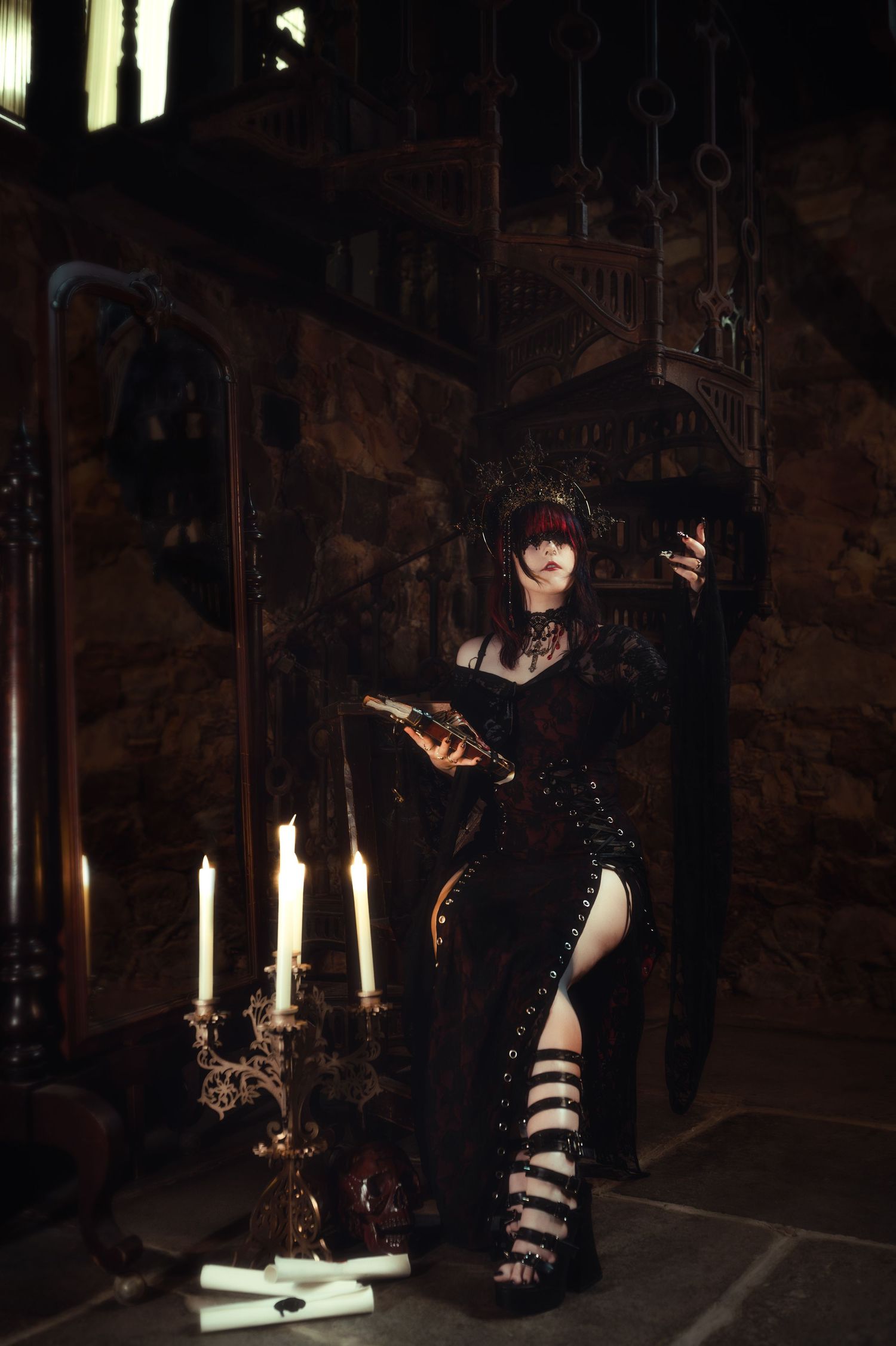 Gothic figure in black lace dress poses with candelabras in a medieval stone chamber.