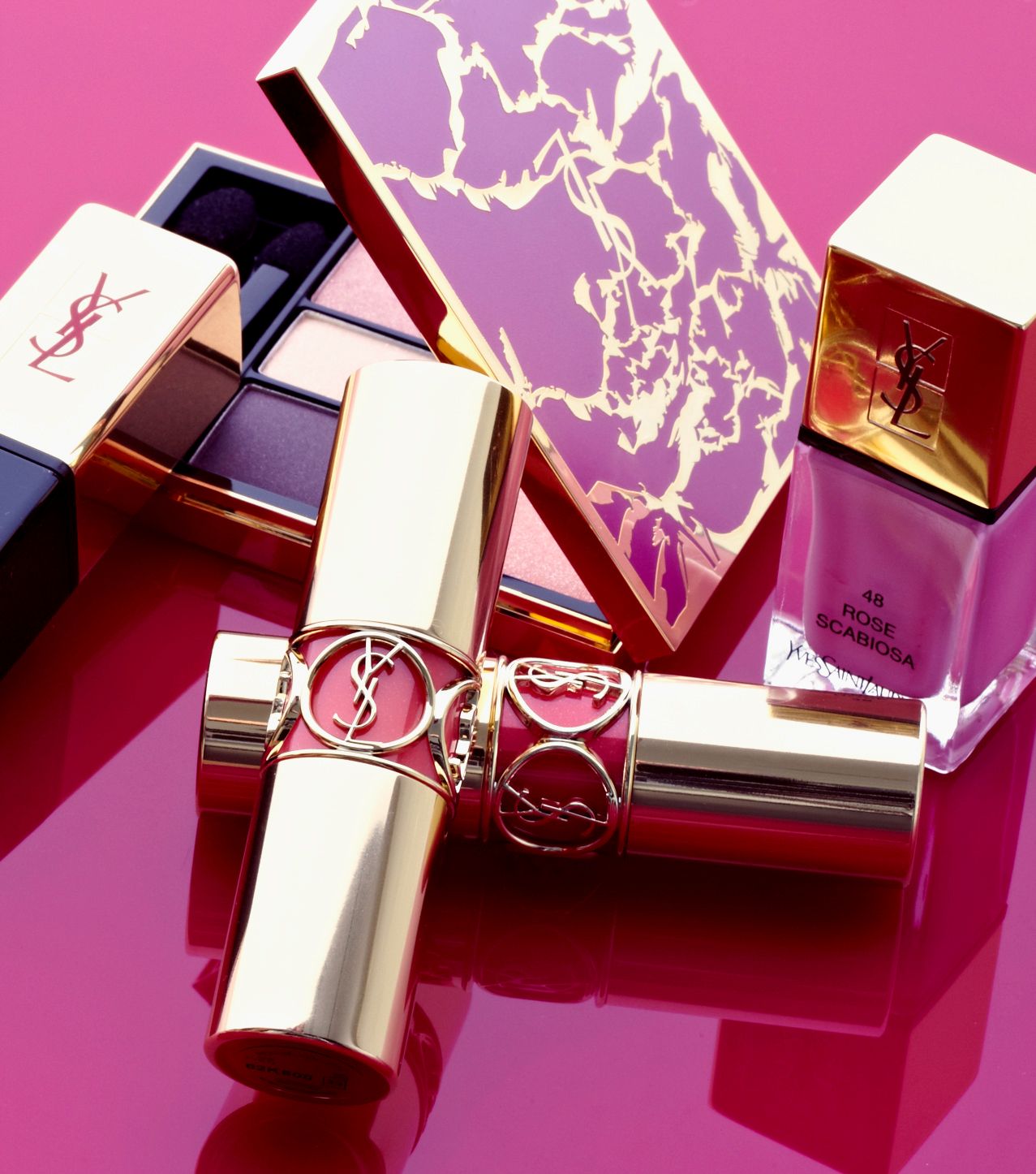 YSL beauty collection featuring lipstick, eyeshadow palette, and nail polish on a pink background.