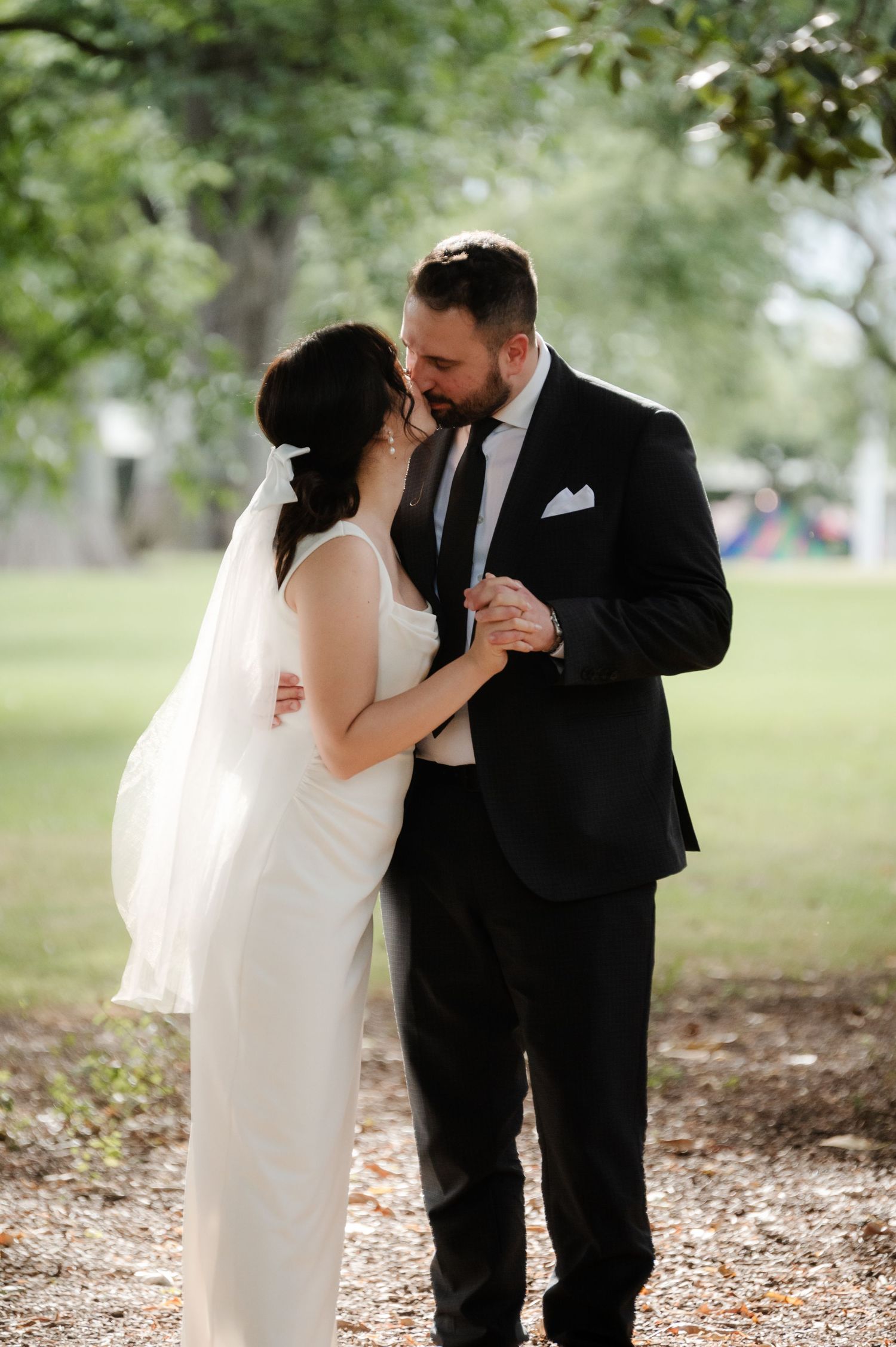Romantic wedding couple embraces under trees during outdoor photo session.