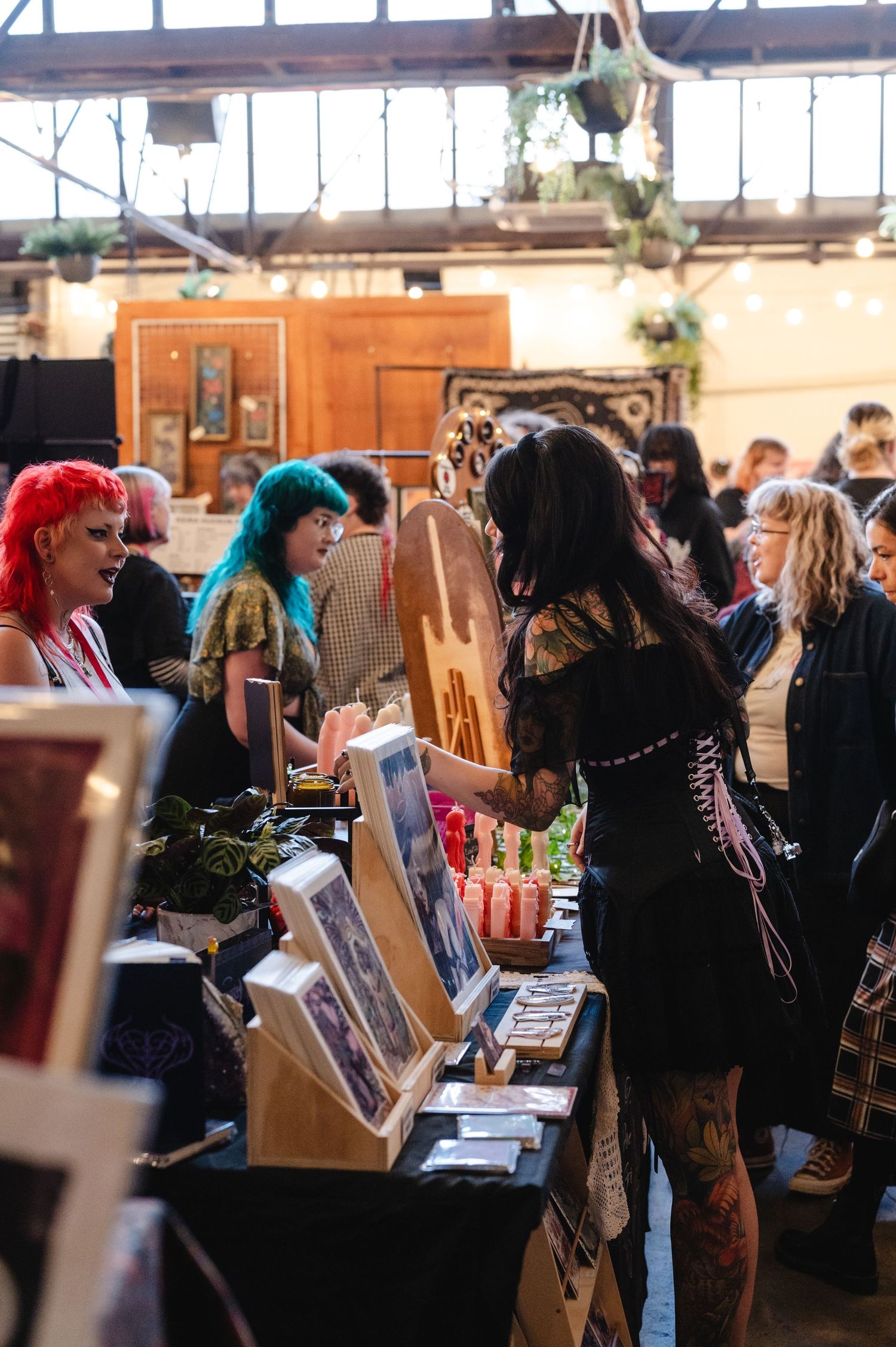 A crowd of people browse through items at an indoor market or craft fair with colorful displays and vendor booths.