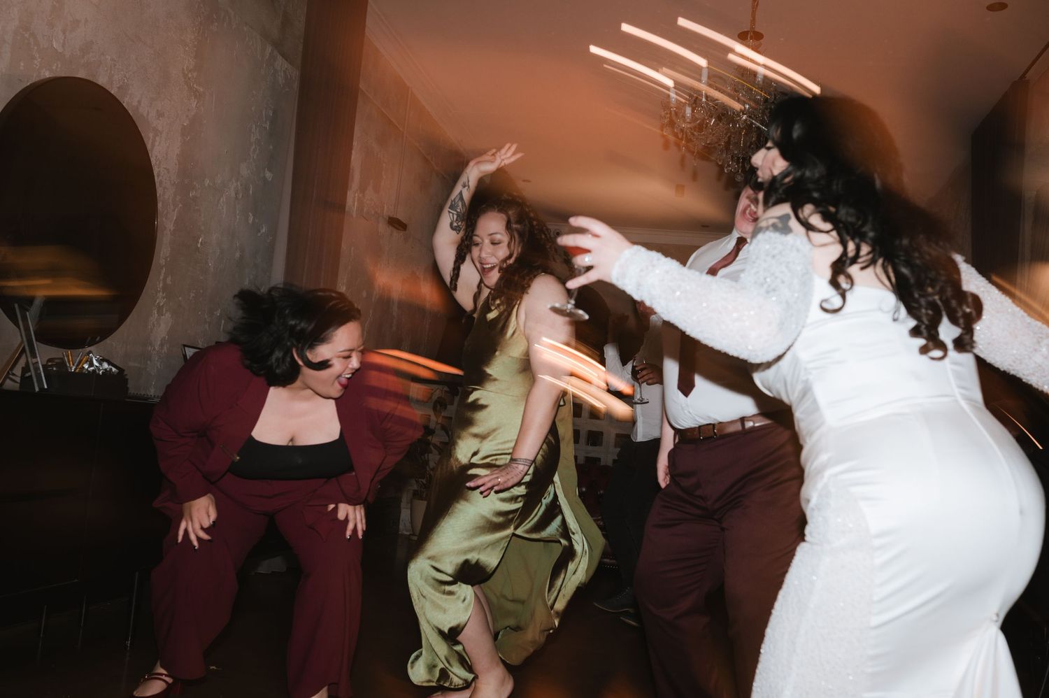 Wedding guests dancing and celebrating on a dimly lit dance floor.