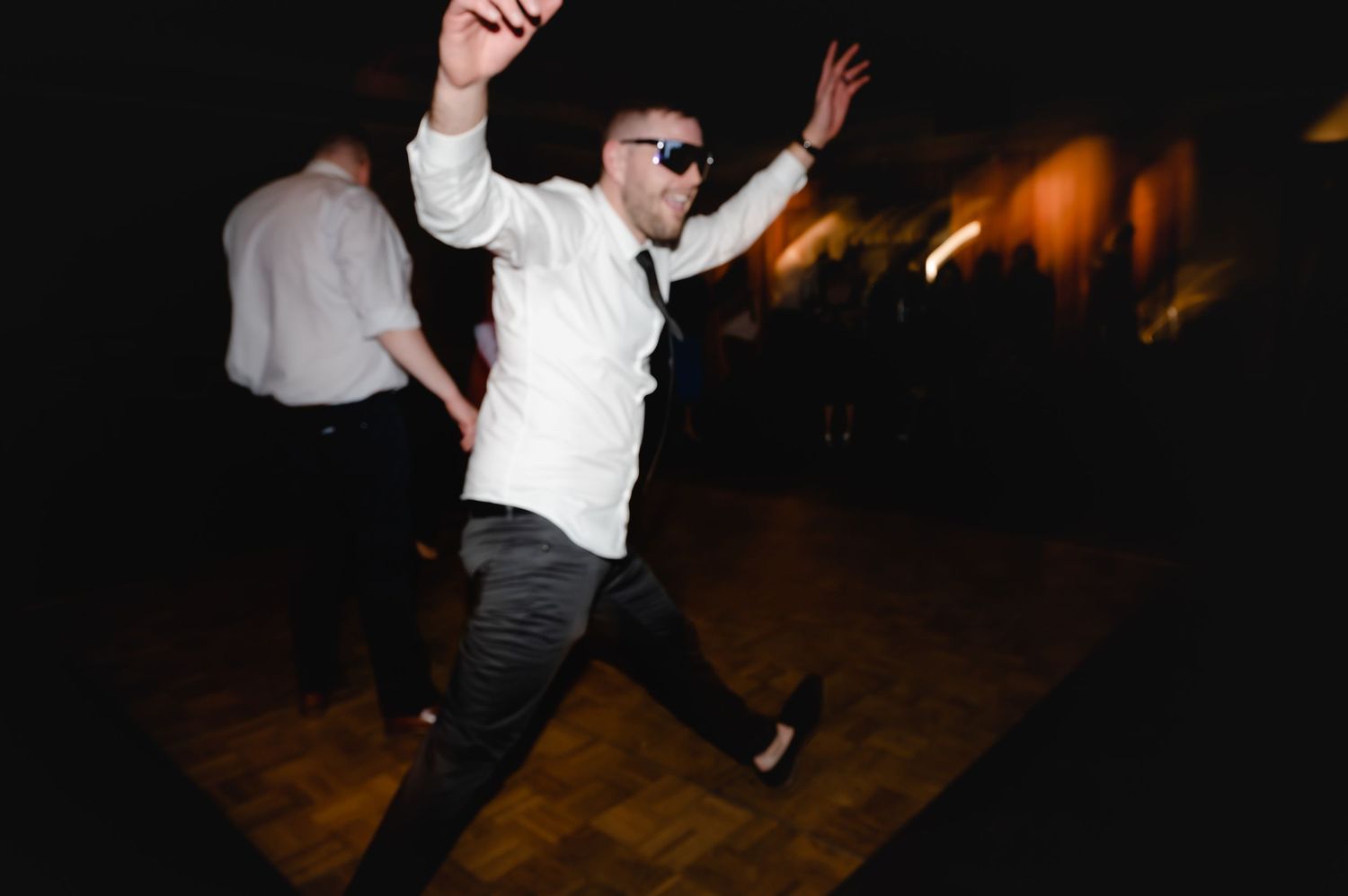 Wedding guests showing off dance moves on a dark dance floor with ambient lighting.