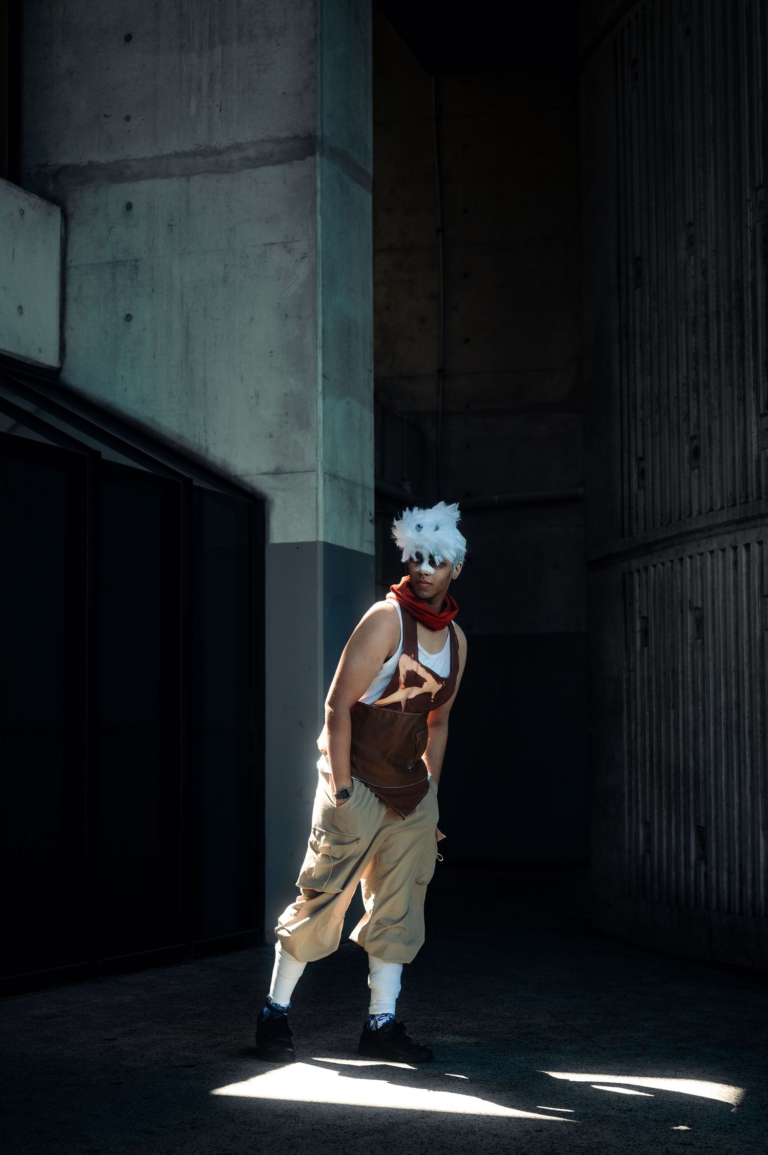 Figure in dramatic lighting poses in concrete urban environment.