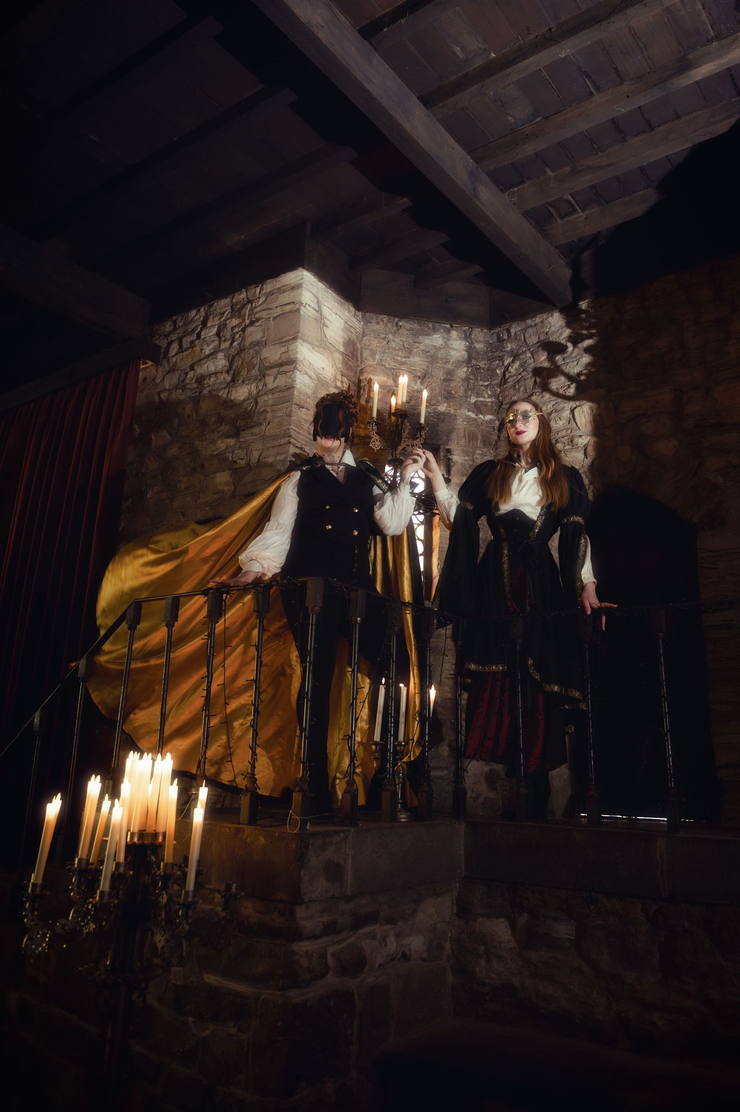 Two performers in medieval costumes stand on a candlelit stone stage holding a candelabra in a dramatic scene.