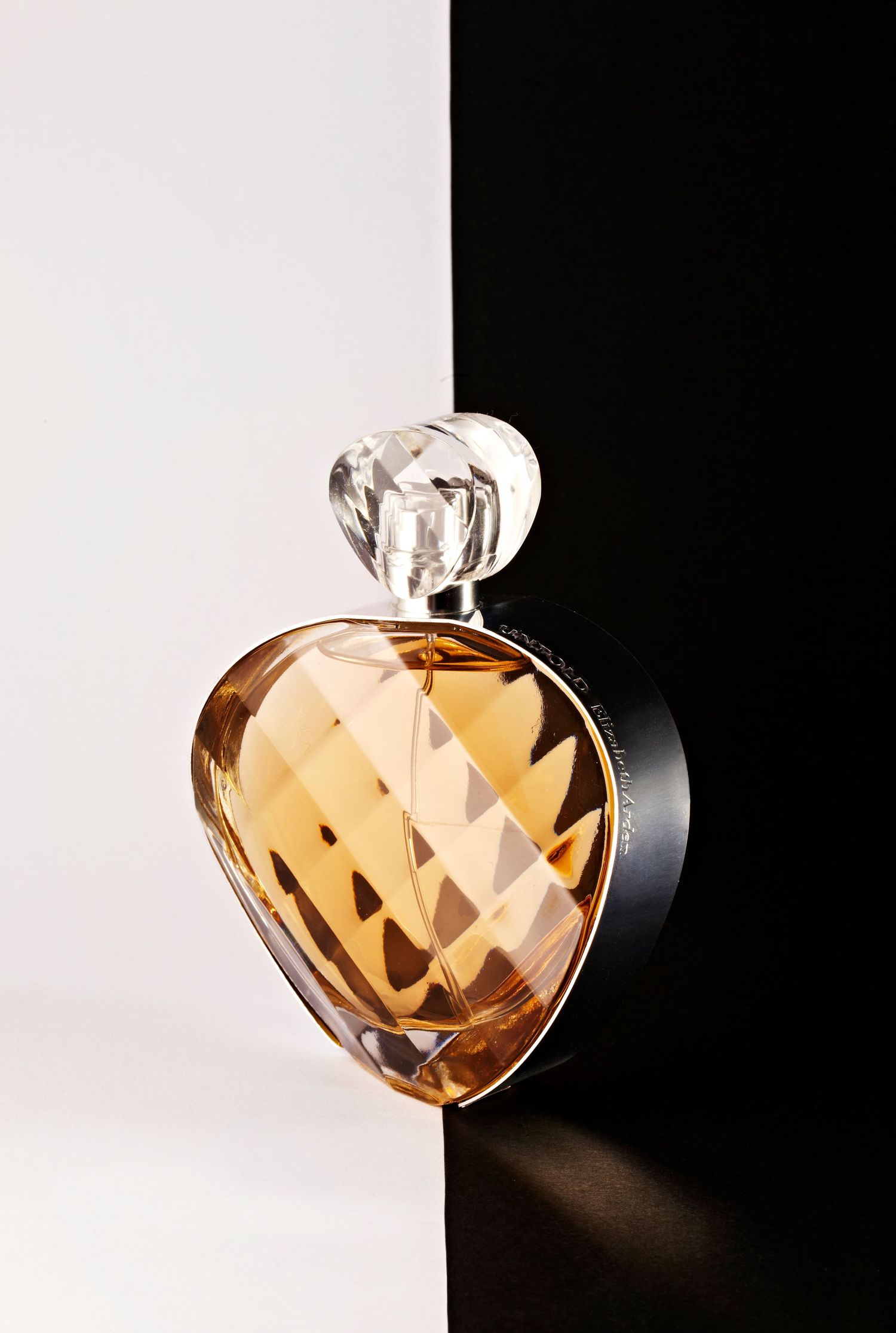 Elegant heart-shaped amber perfume bottle with crystal stopper on black and white background.